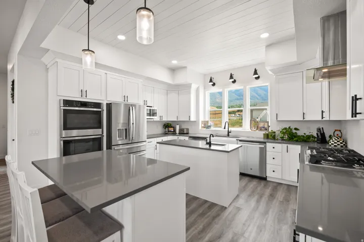 Modern kitchen featuring white shaker cabinetry, stainless steel appliances, dual islands with gray countertops, and wood-finish flooring