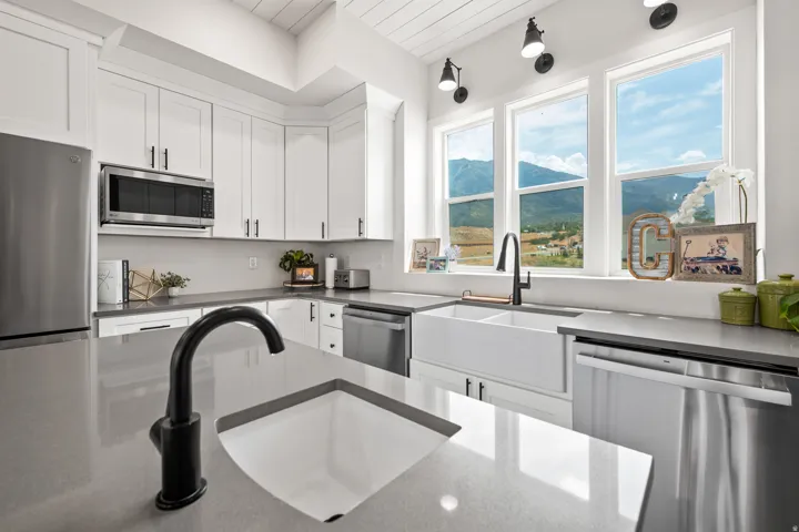 White cabinetry with dark hardware, stainless steel appliances, light gray countertops, and a double basin farmhouse sink with a black faucet
