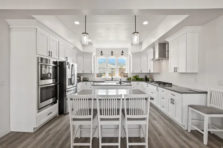 Gourmet kitchen featuring white shaker cabinetry, stainless steel appliances including dual wall ovens, quartz countertops, pendant lighting, and a center island with seating