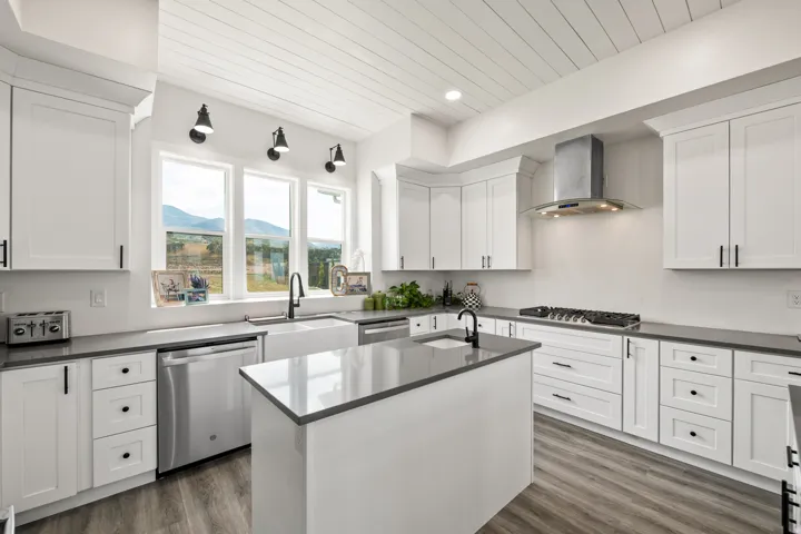 White shaker cabinetry, dark countertops, a central island, stainless steel appliances, and wood-finish flooring