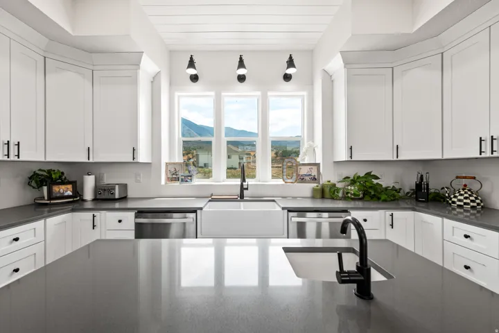 White shaker-style cabinetry, matte black hardware, stainless steel appliances, large farmhouse sink, and gray countertops