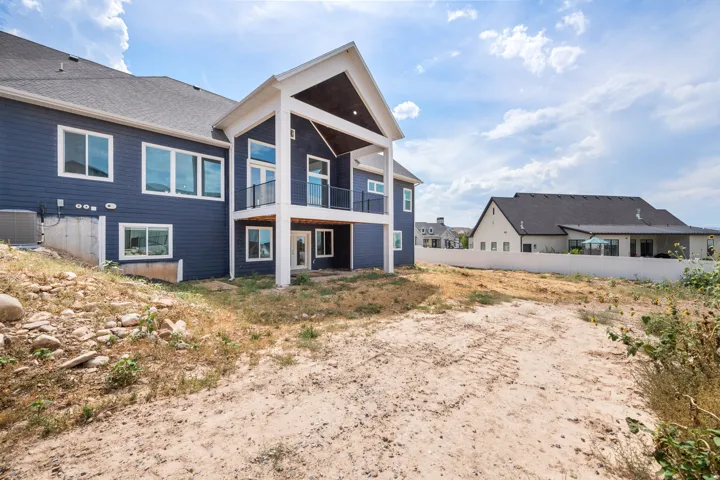 Contemporary exterior with blue siding, a covered balcony featuring black railings, and a lower-level concrete patio