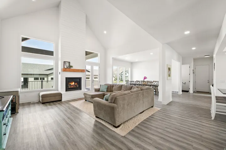 Bright, open-concept living space featuring soaring vaulted ceilings with recessed lighting, wide-plank wood-finish flooring throughout, and a gas fireplace with custom surround