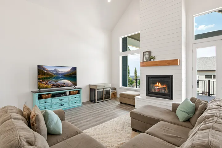 Vaulted ceiling with abundant natural light, fireplace with shiplap surround, wood-finish flooring, and white walls
