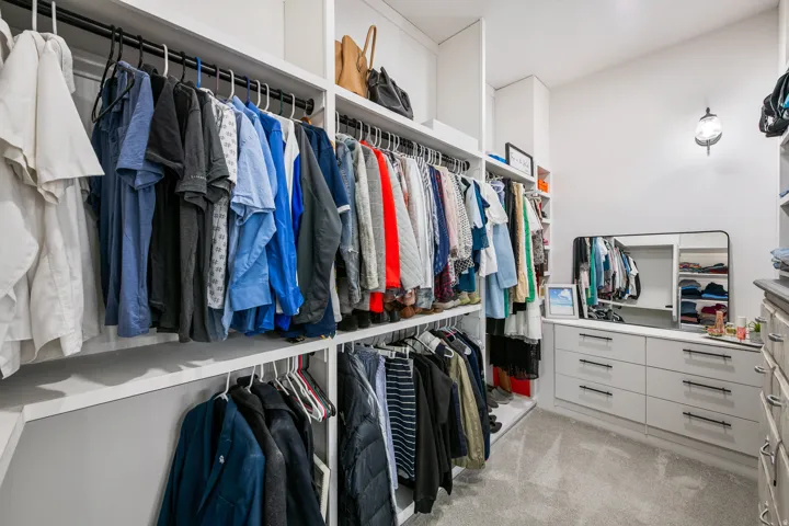 Integrated closet system with multiple hanging rods, built-in shelving, and drawer storage, featuring a carpeted floor and a wall-mounted light fixture