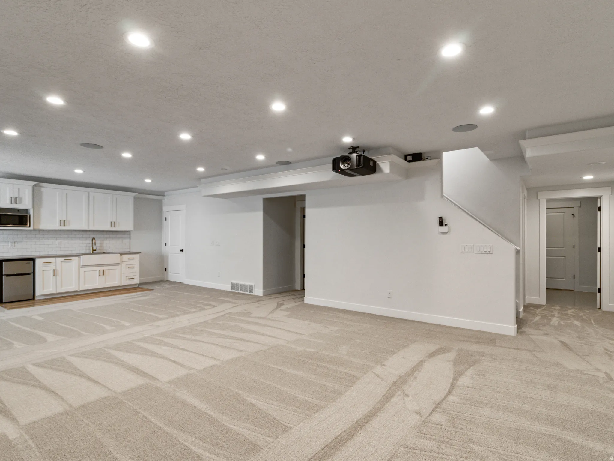 Recessed lighting throughout, built-in projector, wet bar with white cabinetry, built-in microwave, and subway tile backsplash