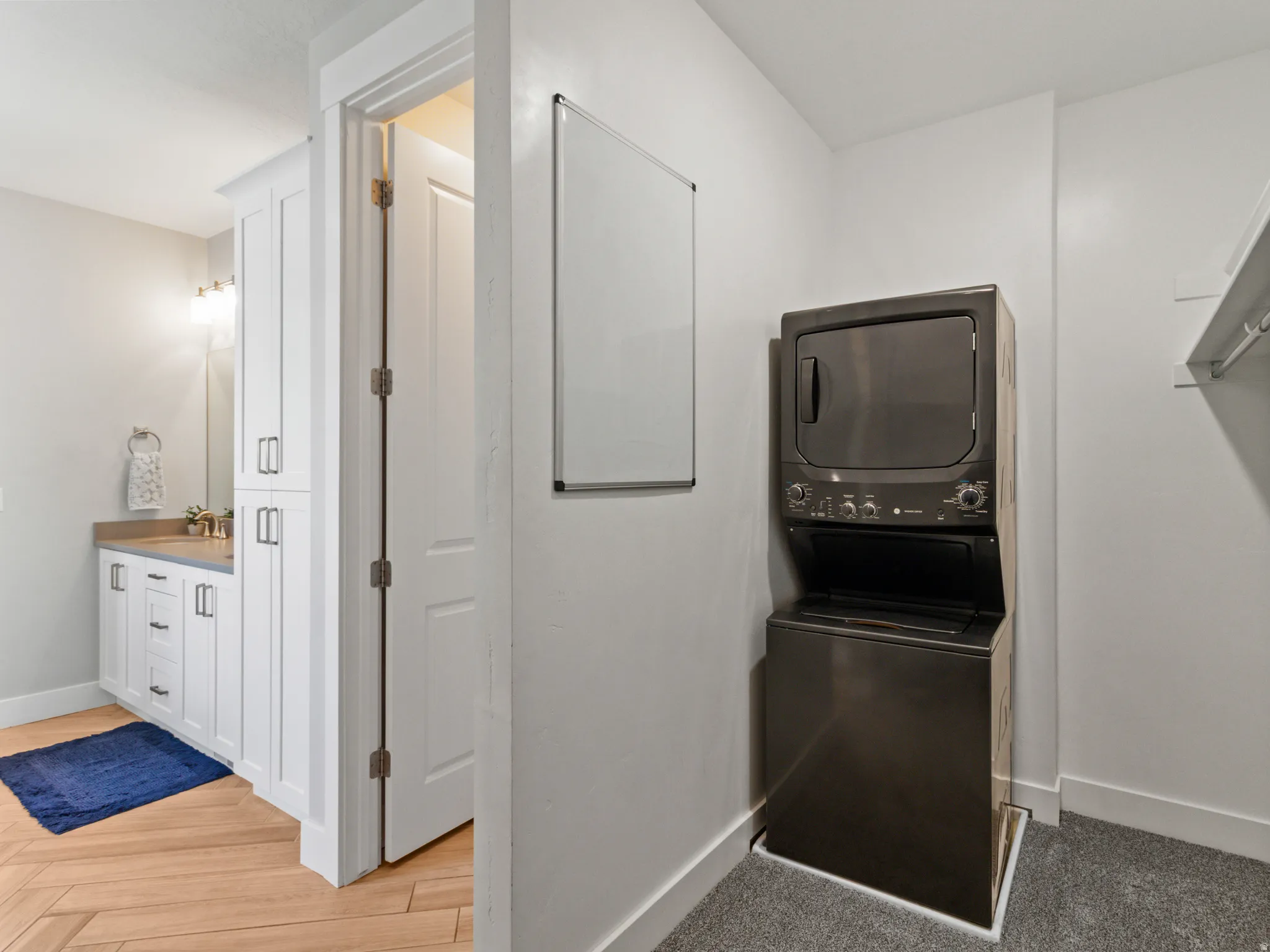 Dedicated laundry room featuring stacked washer and dryer units in sleek black finish, white cabinetry with hardware accents, wood-finish flooring, and neutral wall finishes