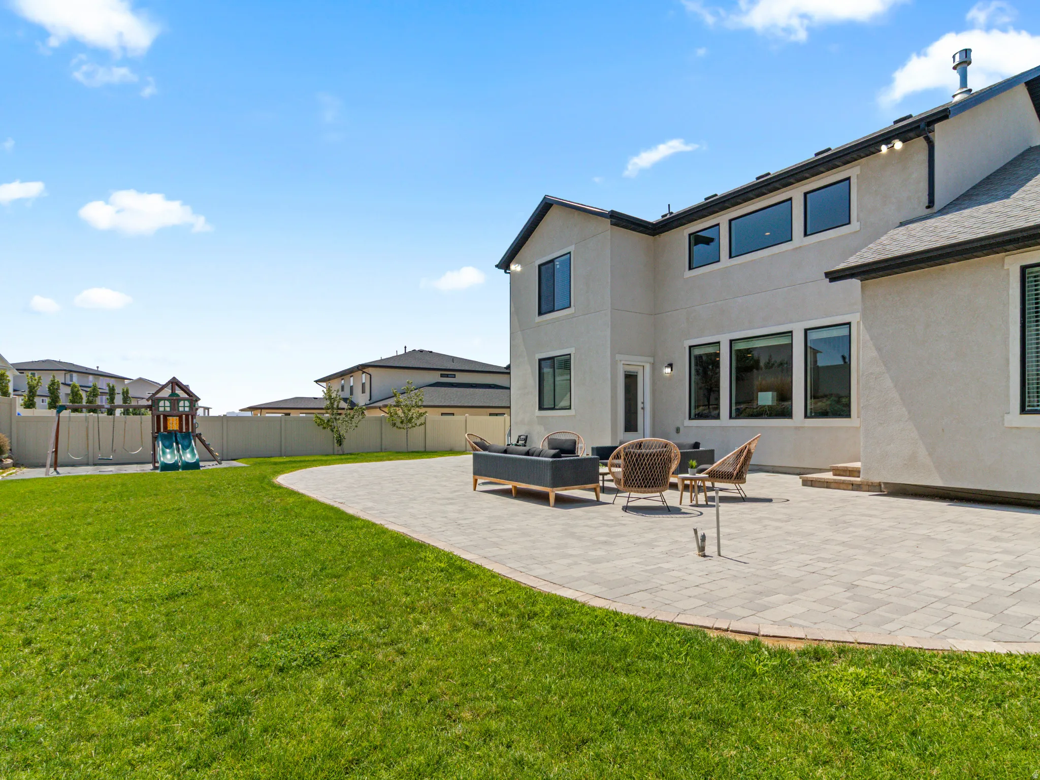 Expansive rear patio featuring large-format pavers with generous entertaining space, overlooking a manicured lawn with mature landscaping