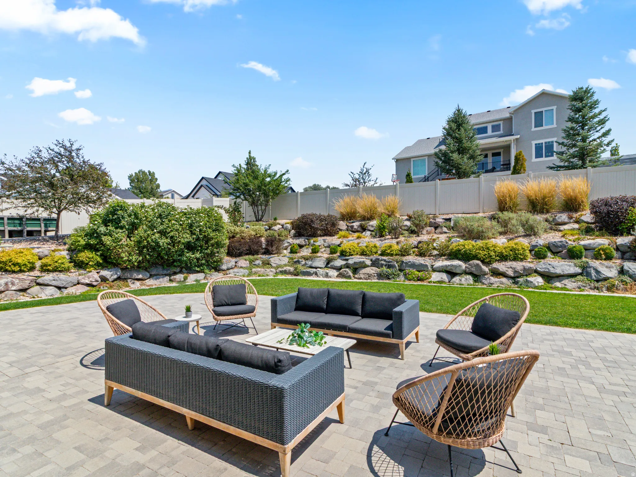 Expansive paver patio with a manicured lawn and a tiered, landscaped retaining wall with various plantings