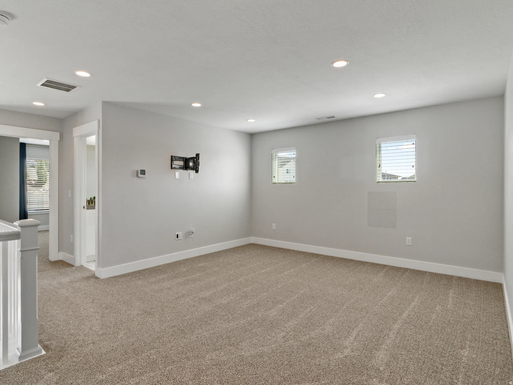 Expansive carpeted area featuring recessed lighting, multiple windows with blinds, a wall-mounted TV bracket, and white trim
