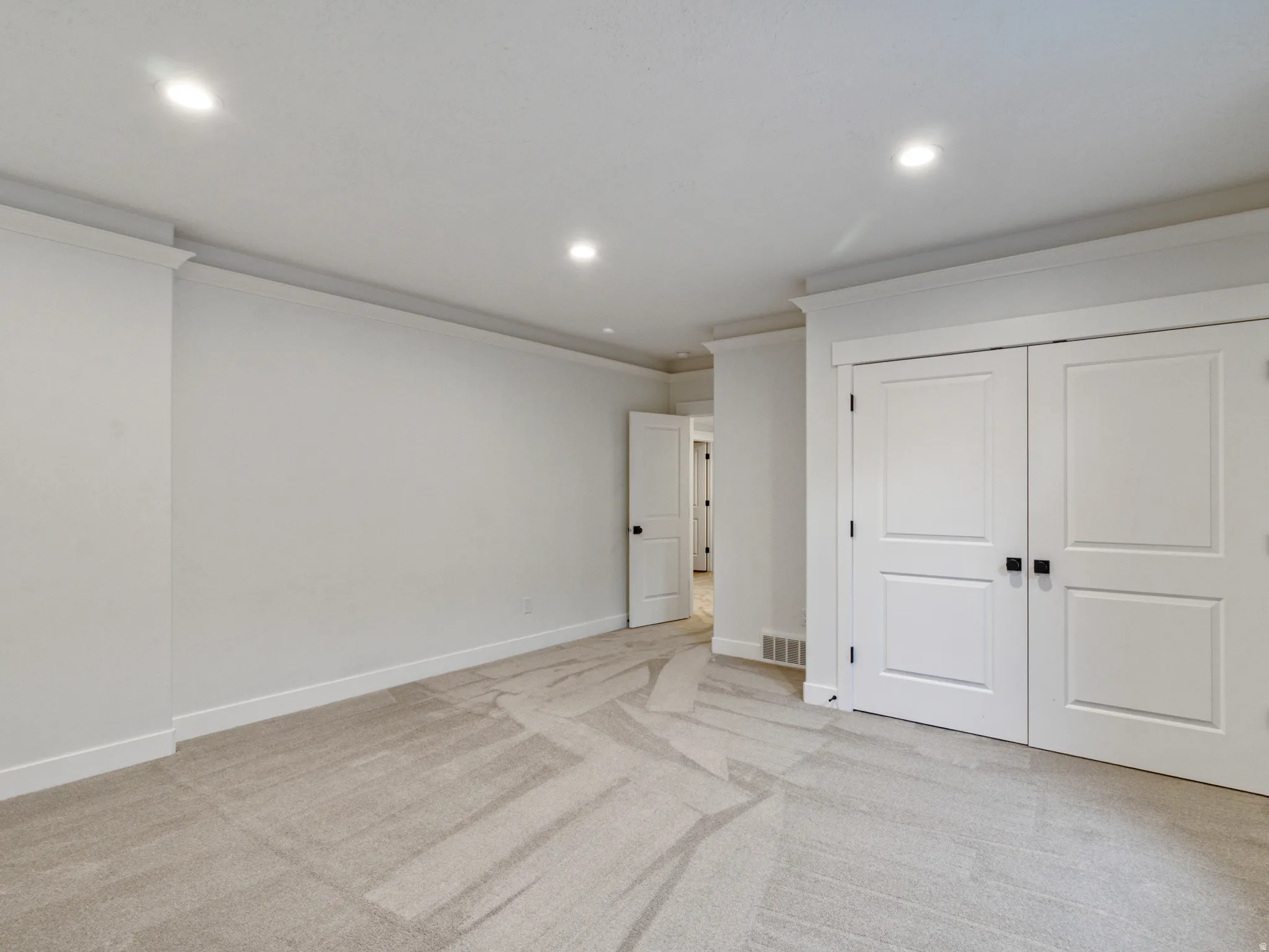 Recessed lighting, crown molding, light-toned carpet flooring, white trim, and white panel doors with matte black hardware