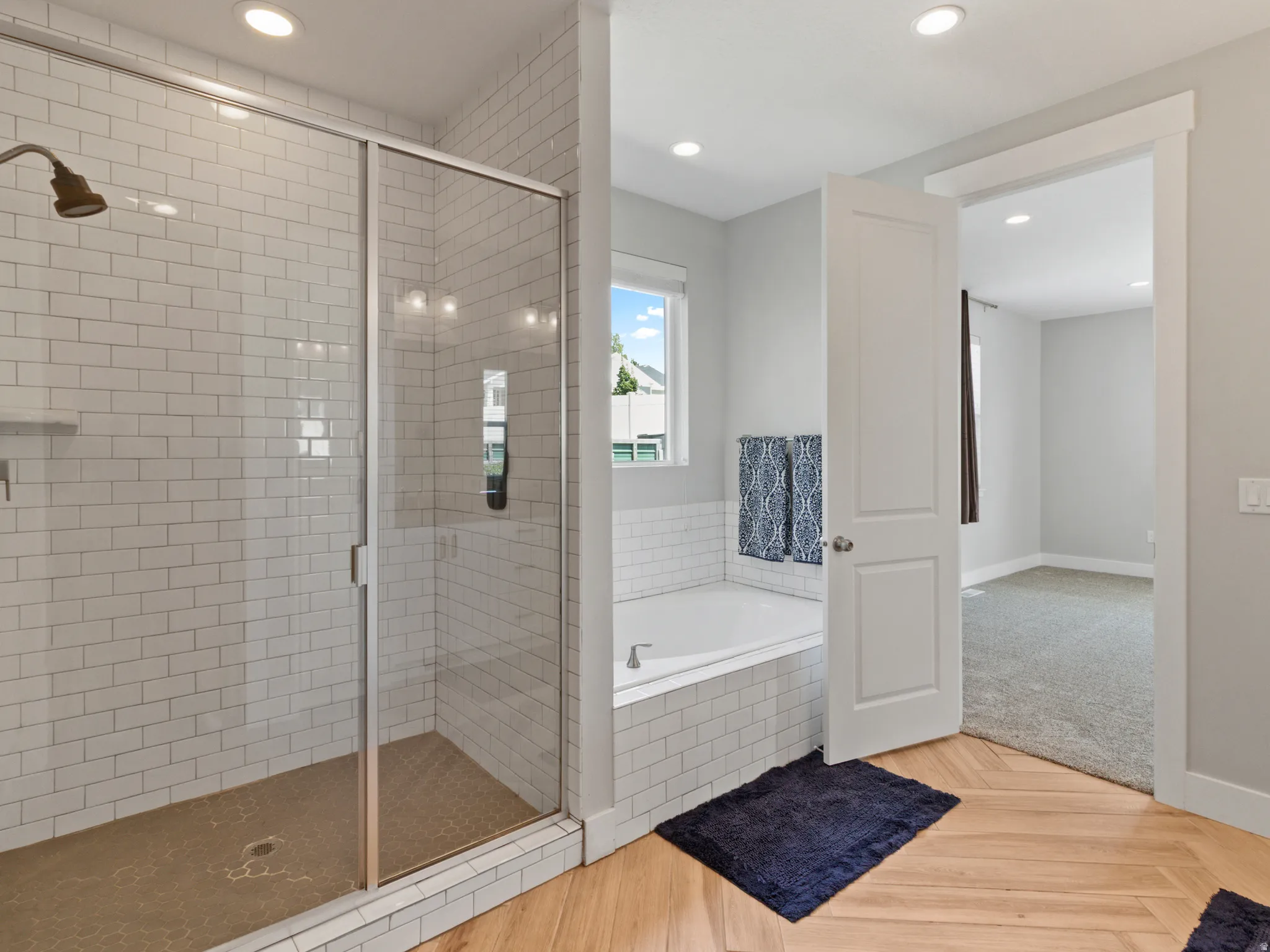 Glass-enclosed shower with subway tile surround, built-in soaking tub, wood-finish herringbone flooring, and recessed lighting