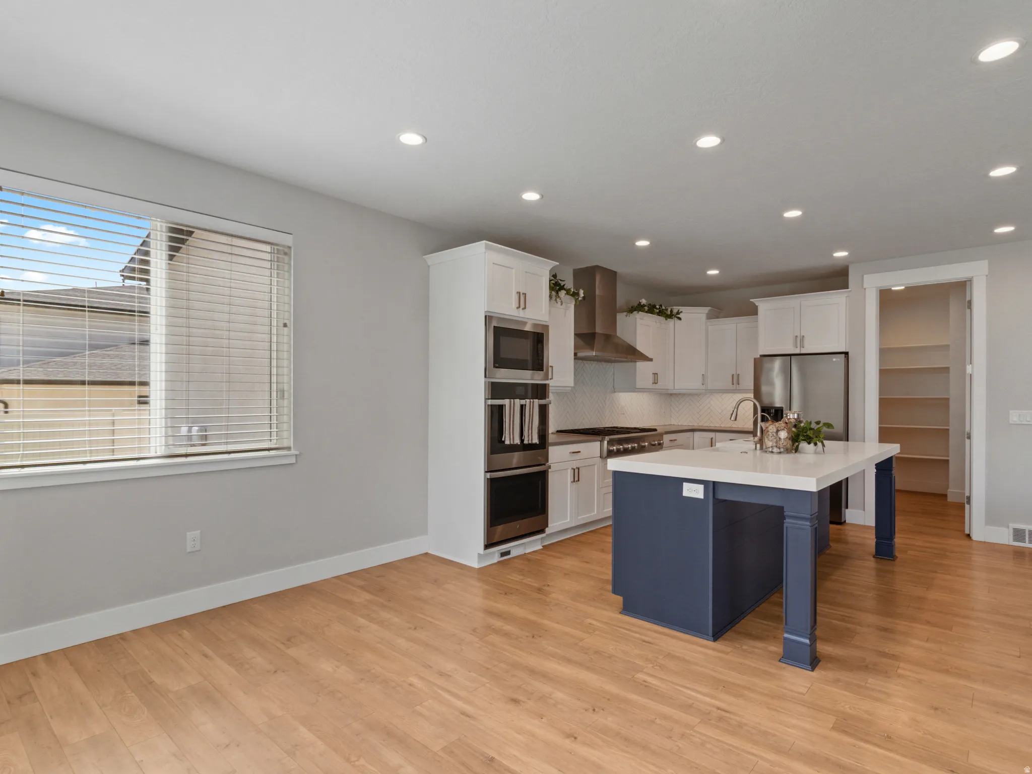 Modern kitchen featuring white cabinetry with integrated appliances, a navy blue center island with waterfall countertop, recessed ceiling lighting, and wood-finish flooring throughout the open-concept space