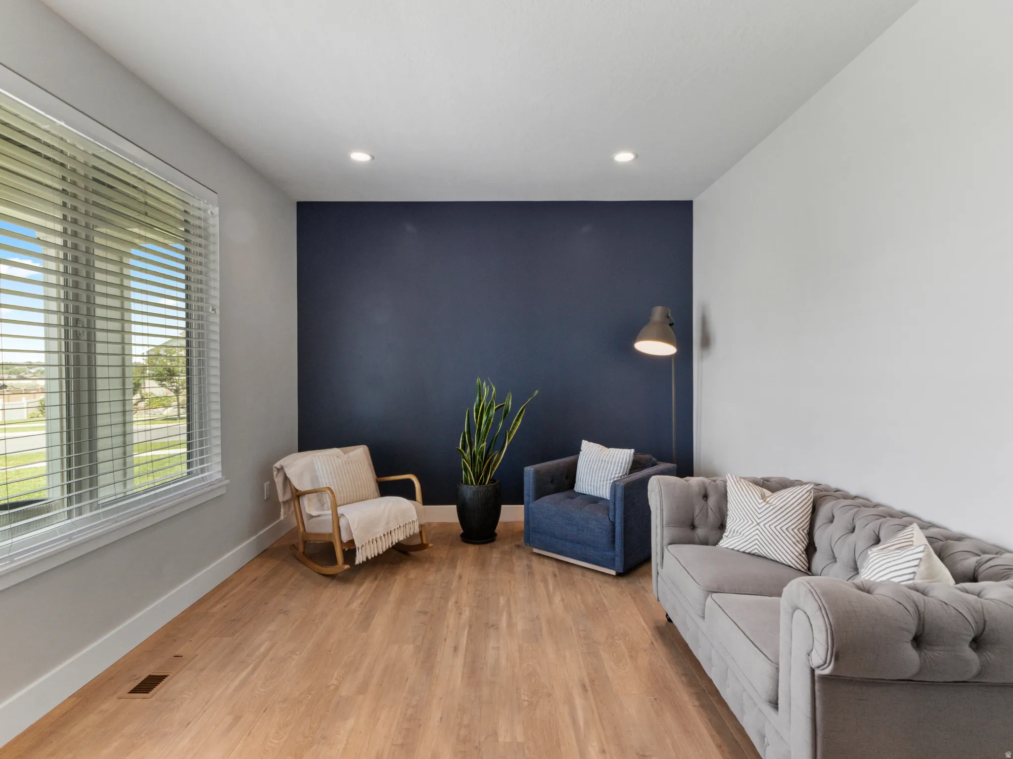 Expansive room featuring wood-finish flooring, a large window with blinds, recessed lighting, and a contrasting accent wall