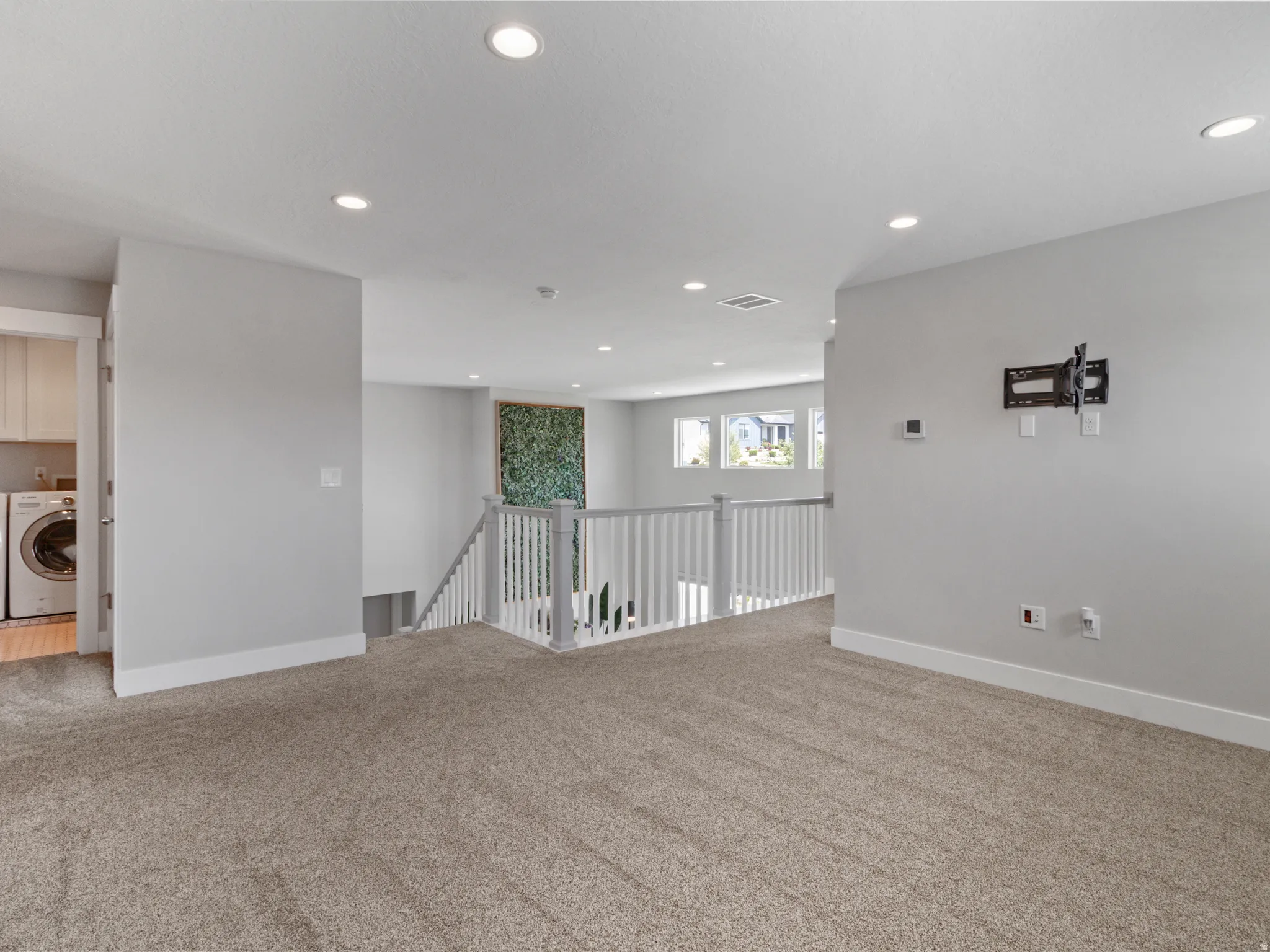 Carpeted loft area featuring recessed lighting, a white spindle railing, and multiple windows