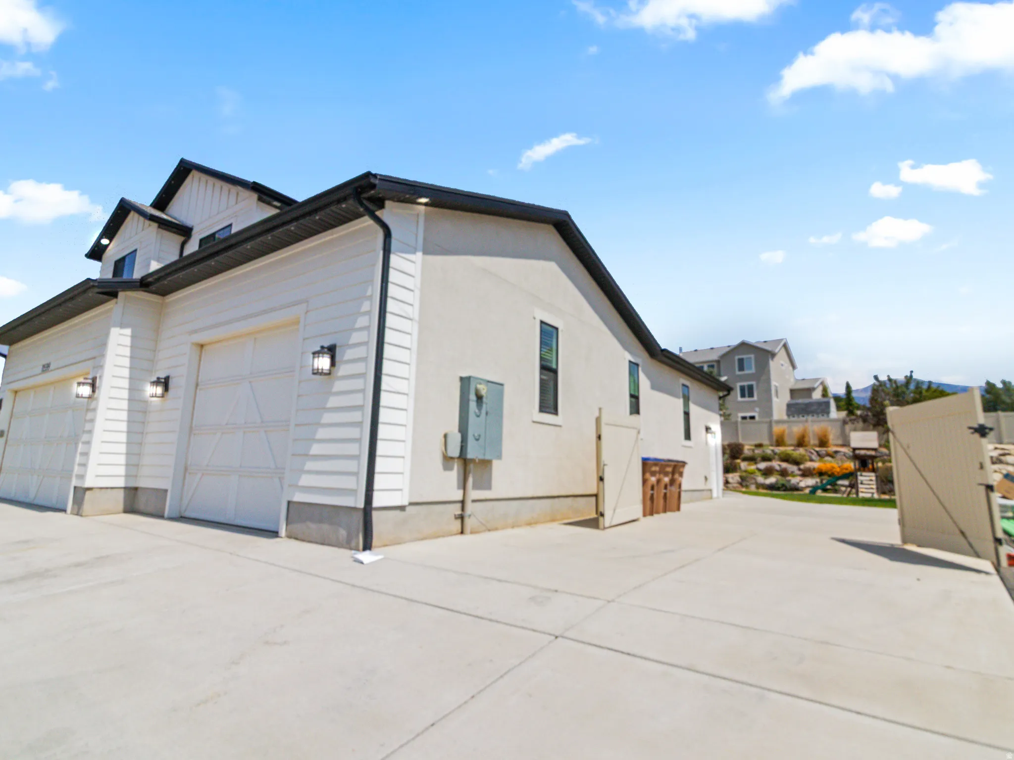 Modern residential architecture featuring a 5-car garage with paneled doors, clean horizontal siding in neutral tones, and a contemporary roofline with mixed materials