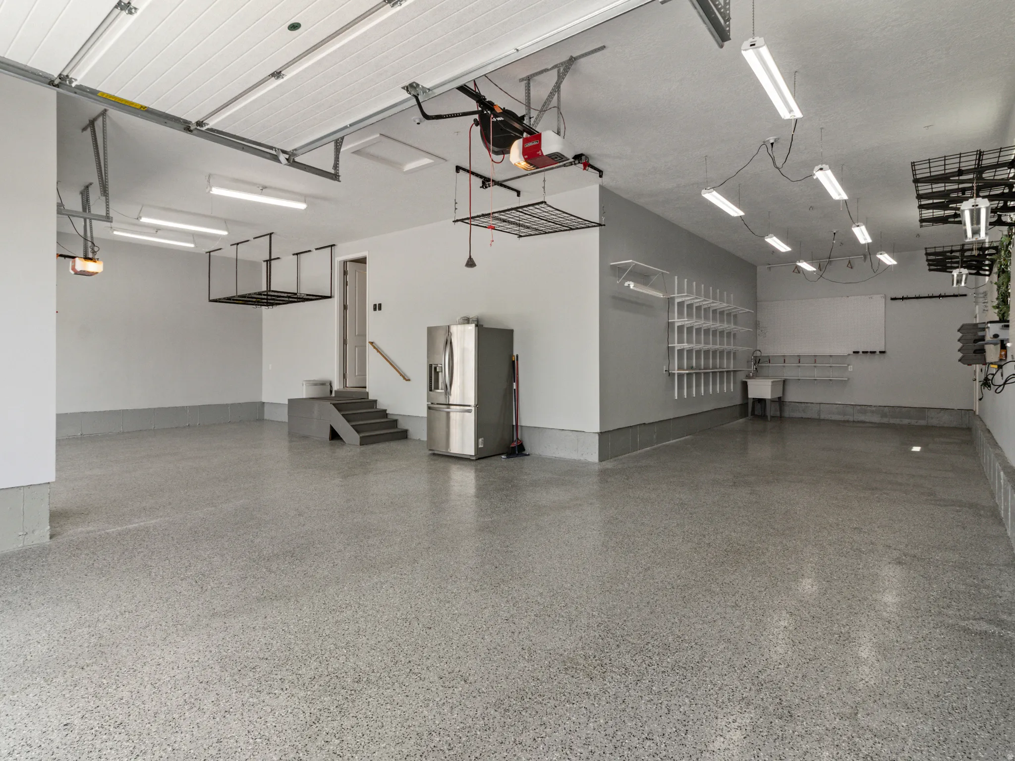 Large garage space featuring an epoxy-coated concrete floor, overhead storage racks, a utility sink, and wall-mounted shelving