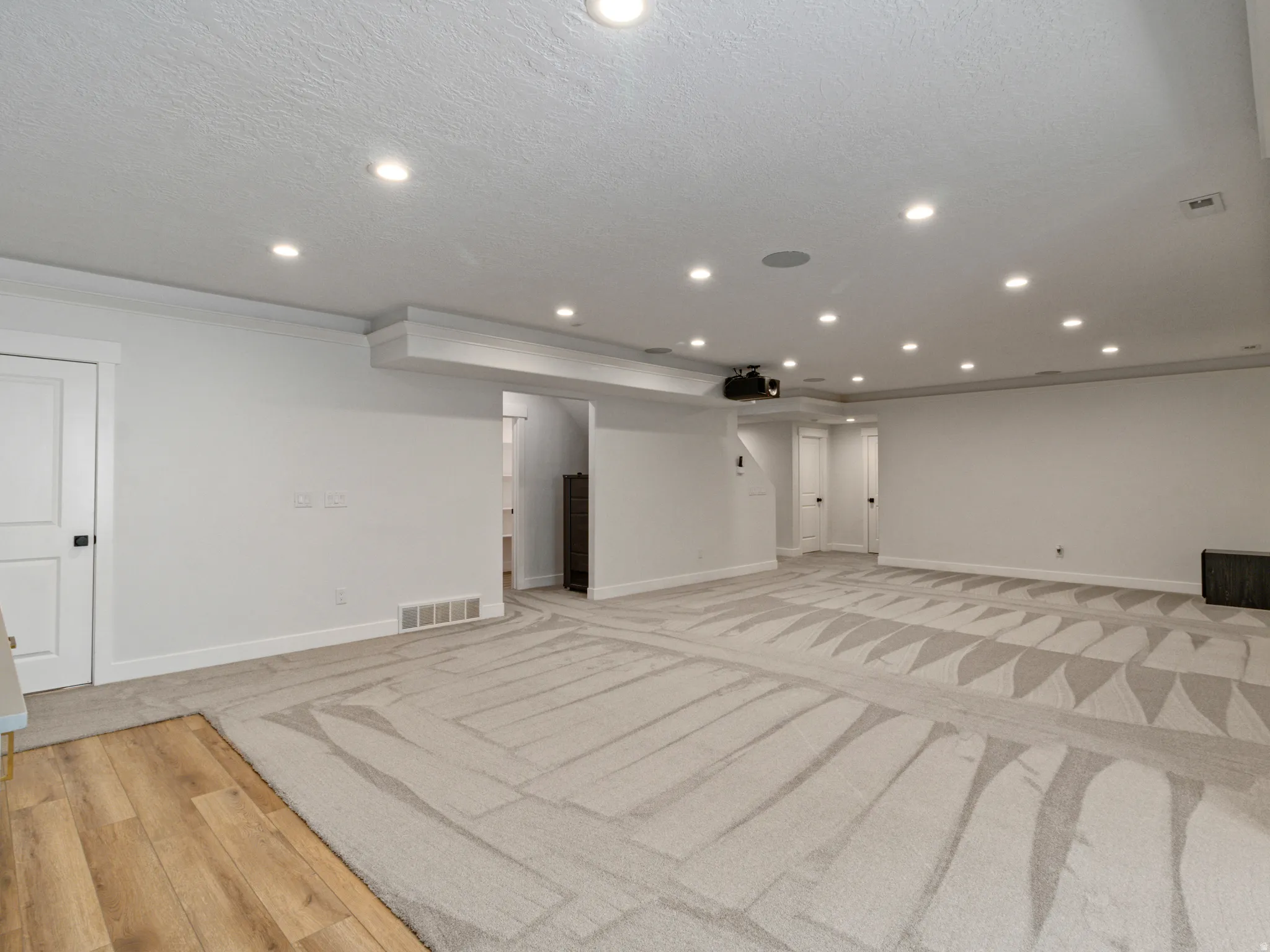 Recessed ceiling lighting, projection system, light-toned patterned carpeting, wood-finish flooring, and white interior doors