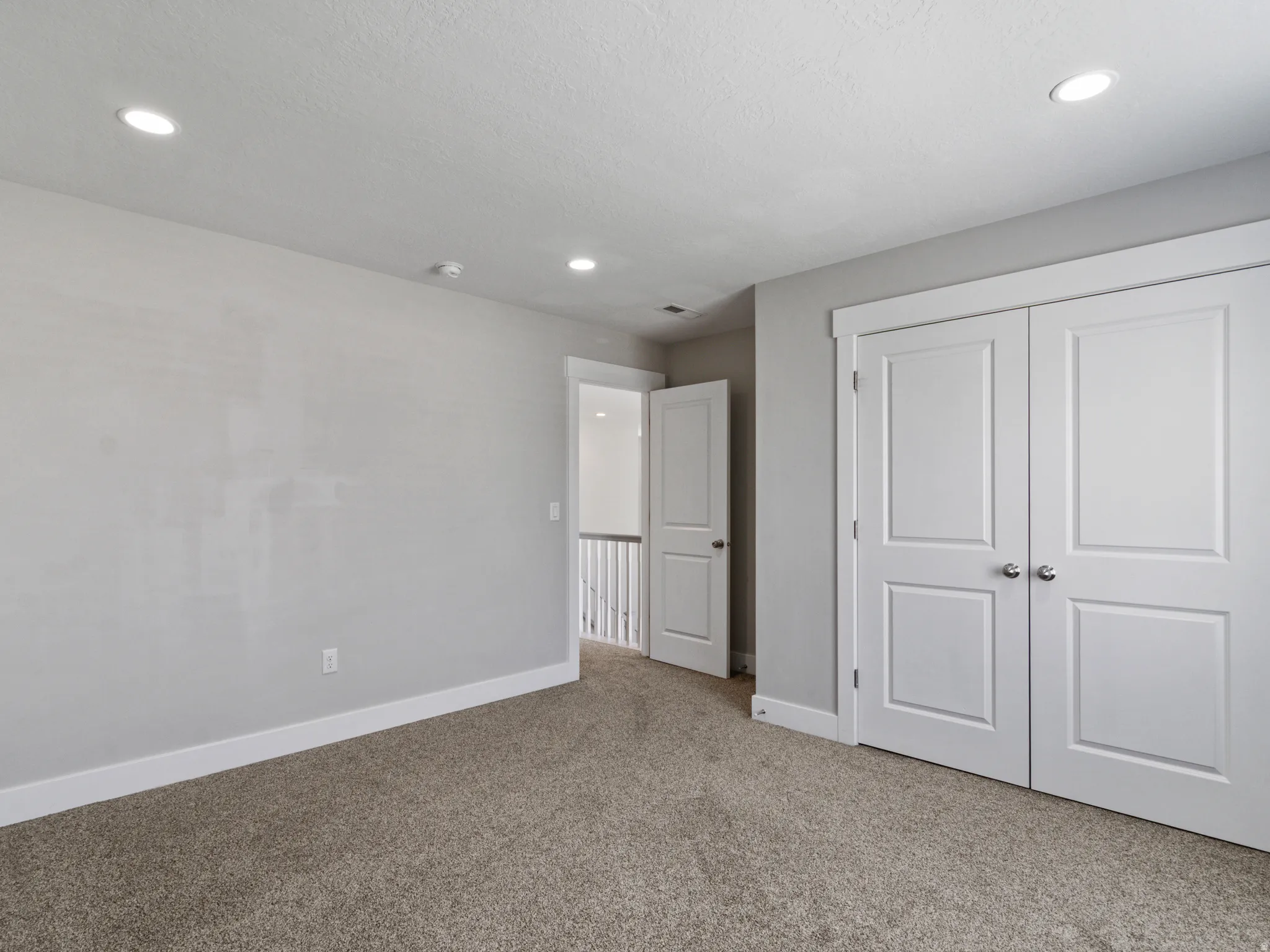Neutral-toned carpeting, recessed ceiling lighting, white trim and baseboards, and paneled doors with brushed nickel hardware