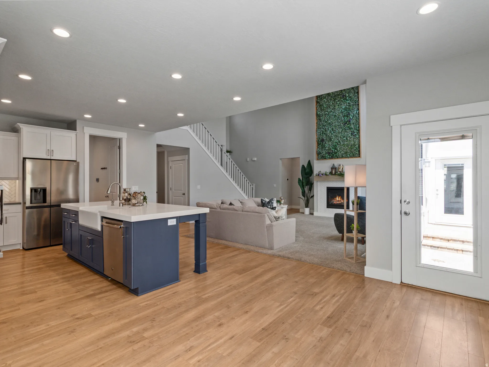 Open-concept living space featuring a chef's kitchen with a navy island, stainless steel appliances, and white cabinetry, complemented by wood-finish flooring throughout