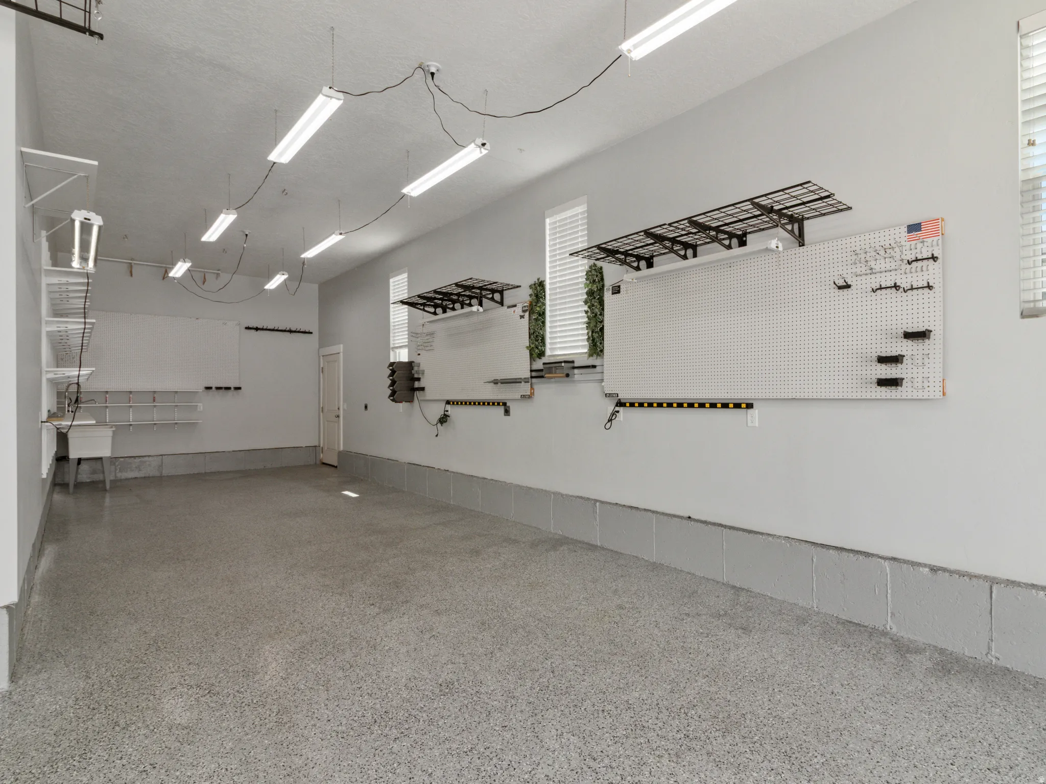 Garage with epoxy-coated flooring, multiple fluorescent lighting fixtures, built-in shelving, and utility sink