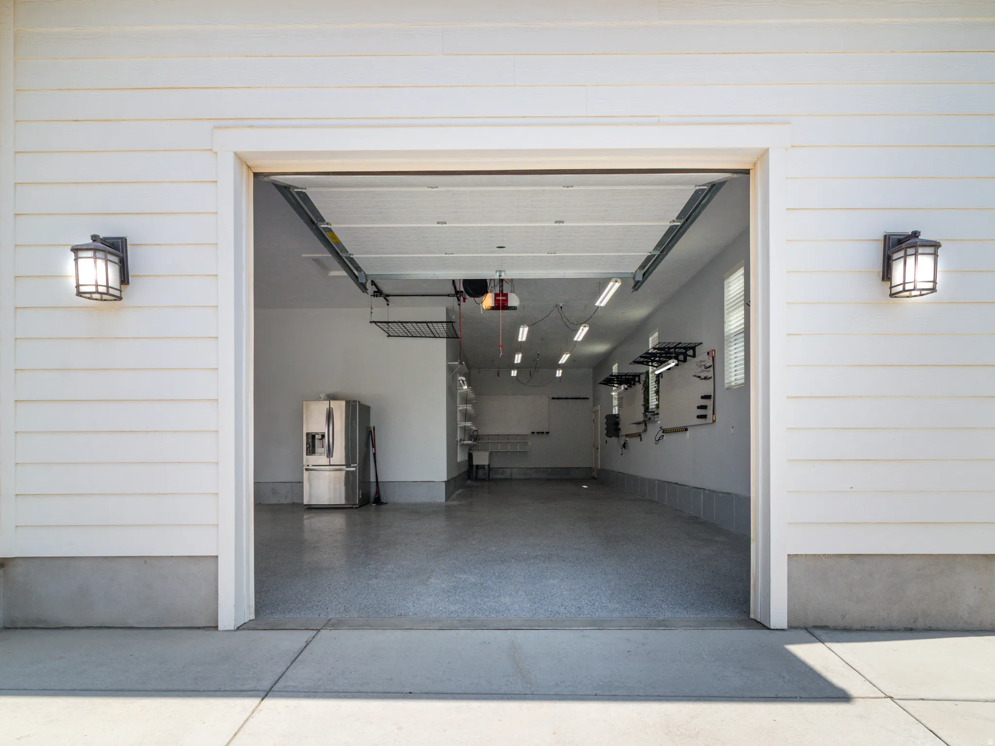 Attached garage with white horizontal siding, two exterior sconce lights, and a textured concrete floor