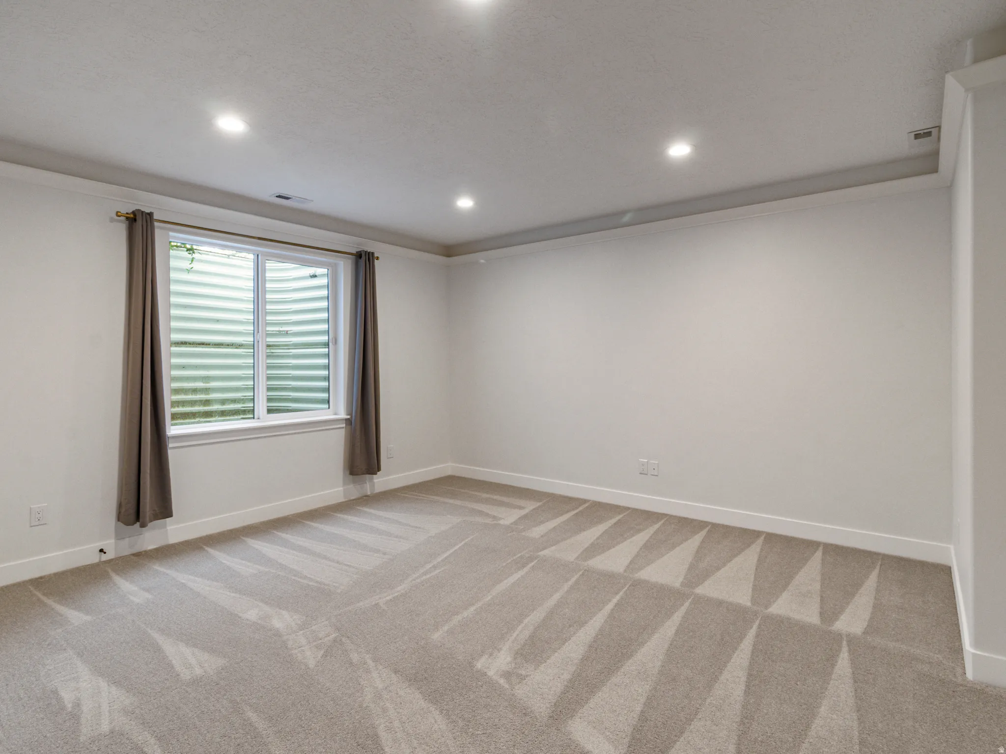 Recessed ceiling lighting, crown molding, a window with a well view, and neutral-toned carpeting