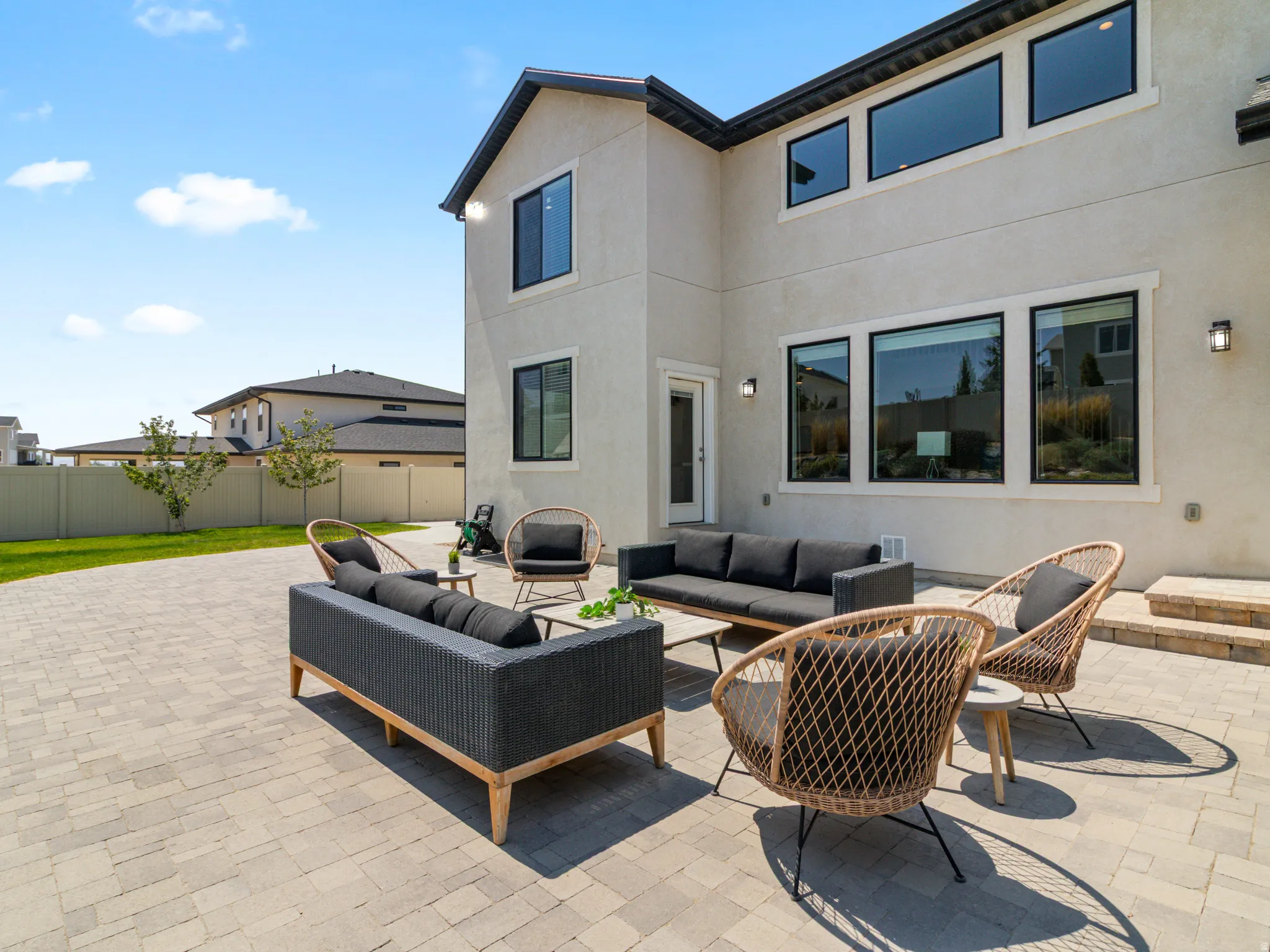 Exterior featuring a paver patio, stucco finish, multiple large windows, a single-light exterior door, and exterior wall sconces