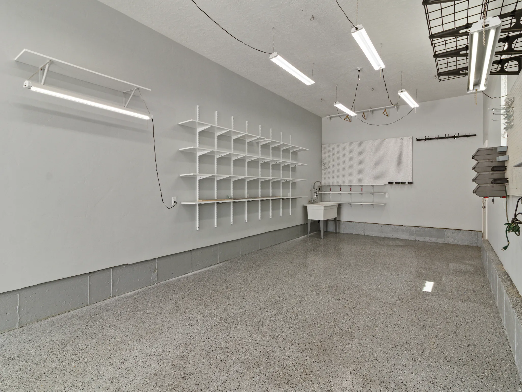 Bright, versatile commercial or retail space featuring epoxy flooring, white wall surfaces, and comprehensive built-in shelving with gridded organization system