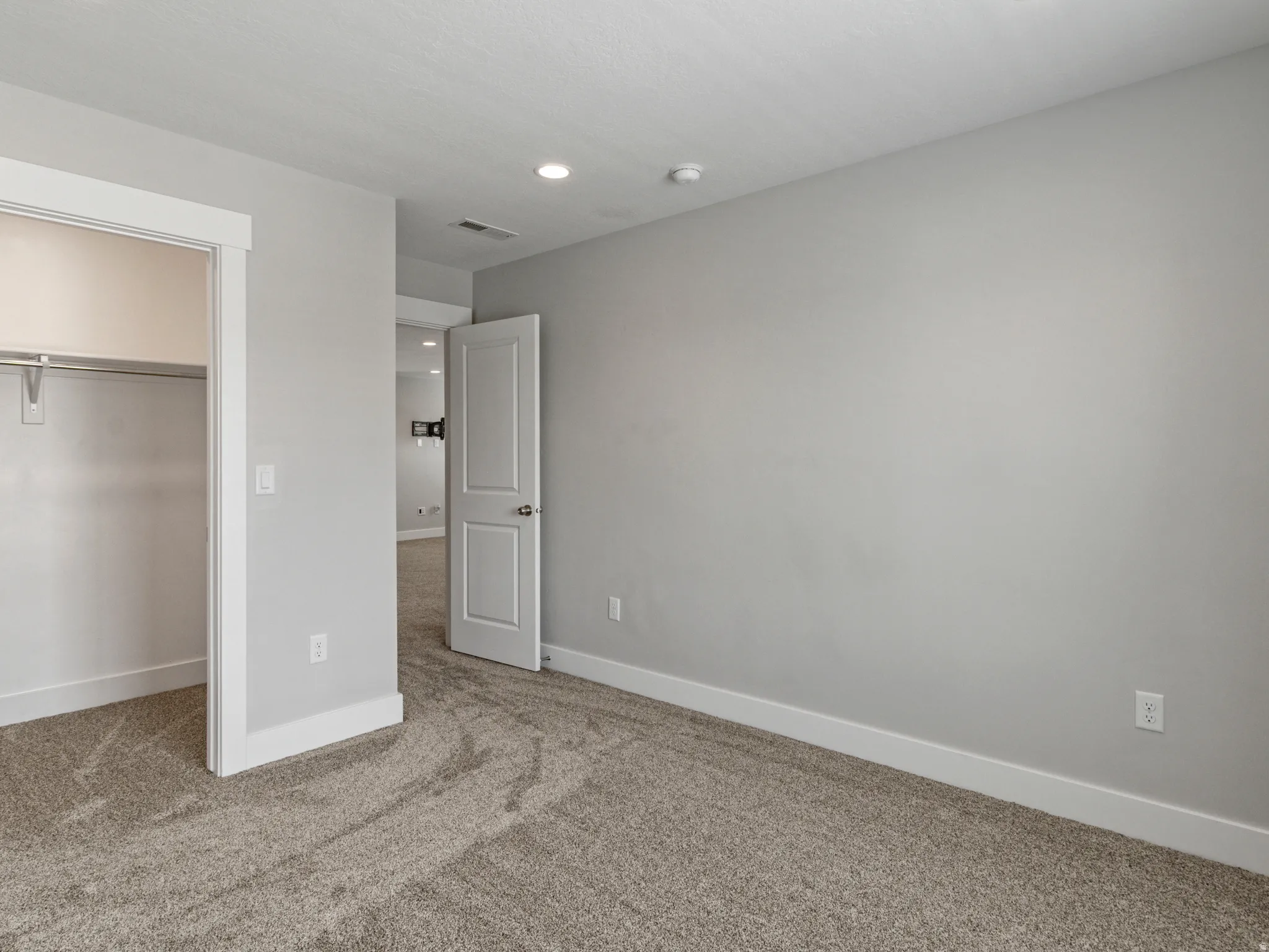Neutral-toned wall paint with recessed lighting, complemented by a walk-in closet featuring a clothes rod