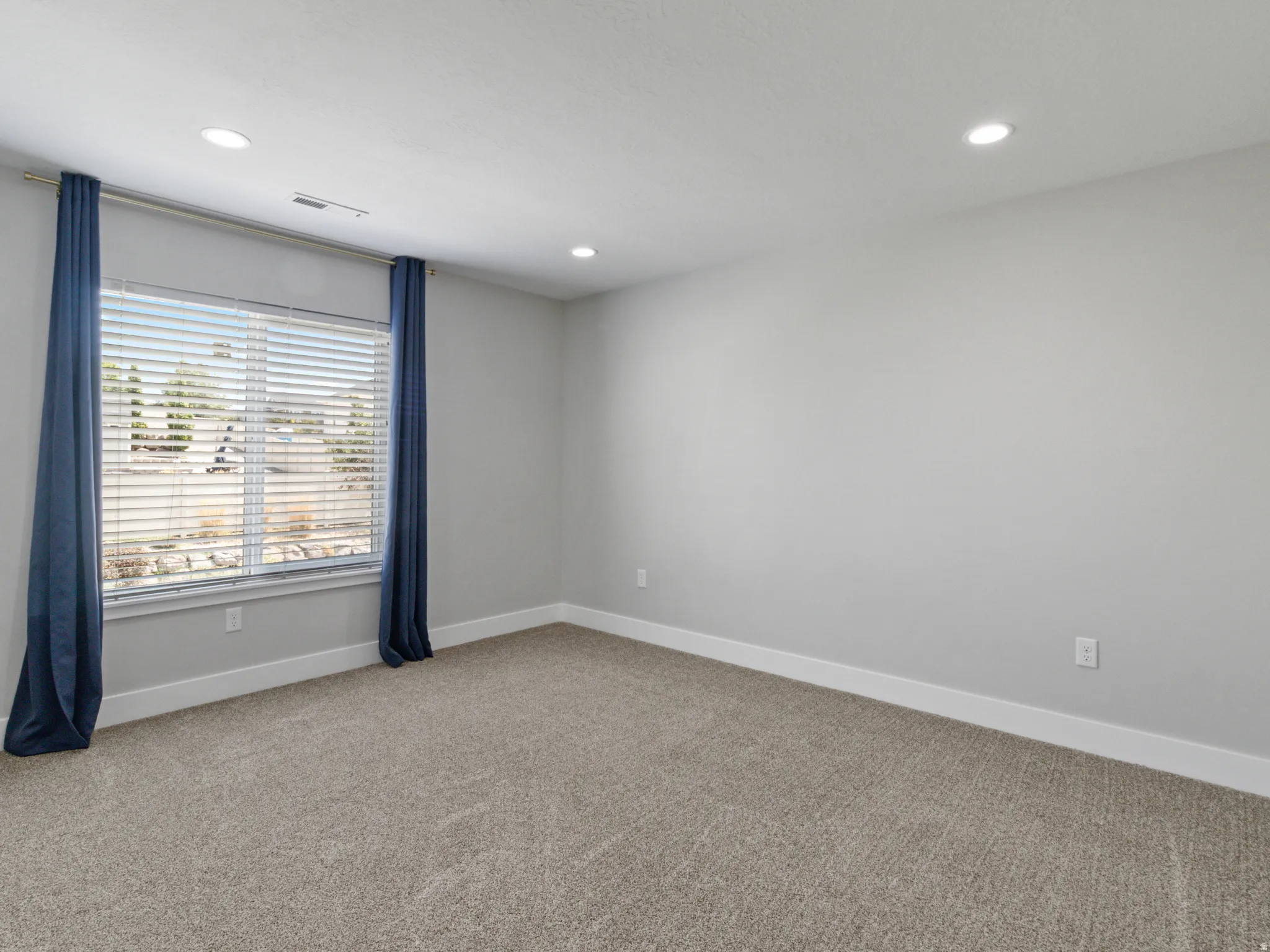Recessed ceiling lighting, textured carpeting, large window with blinds, and light-toned wall finishes