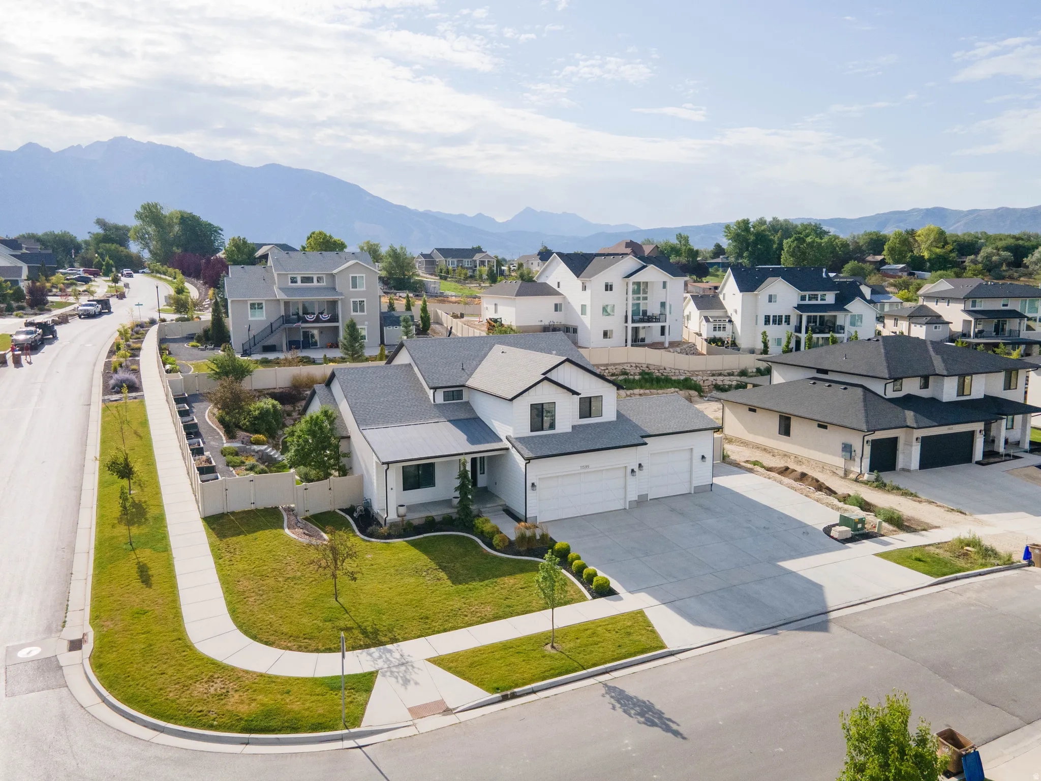 Contemporary white exterior with dark trim accents, 5-car garage, concrete driveway, and a manicured lawn