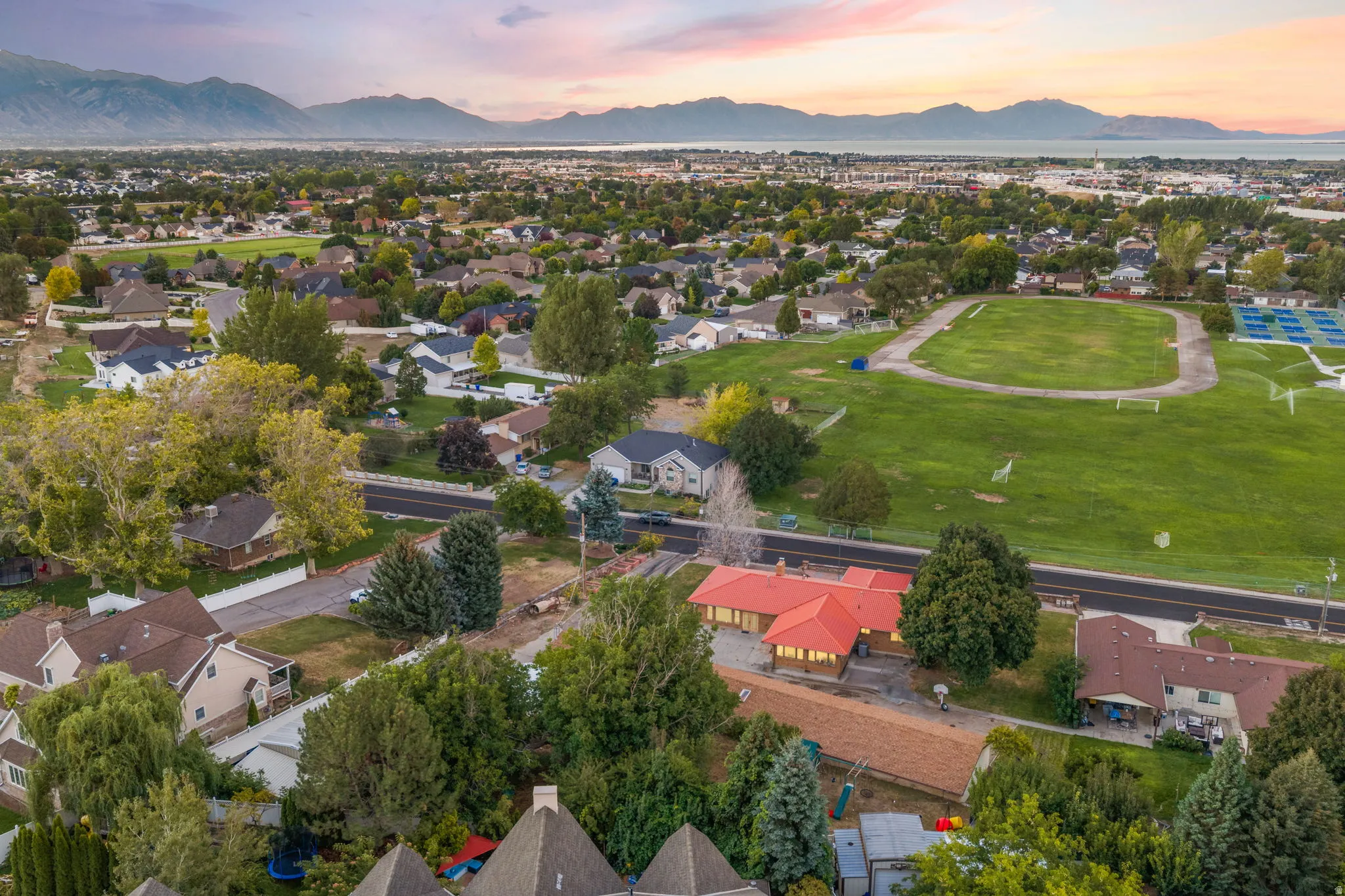Expansive suburban landscape featuring a prominent red-roofed structure, surrounded by mature trees, a green athletic field, and distant mountains