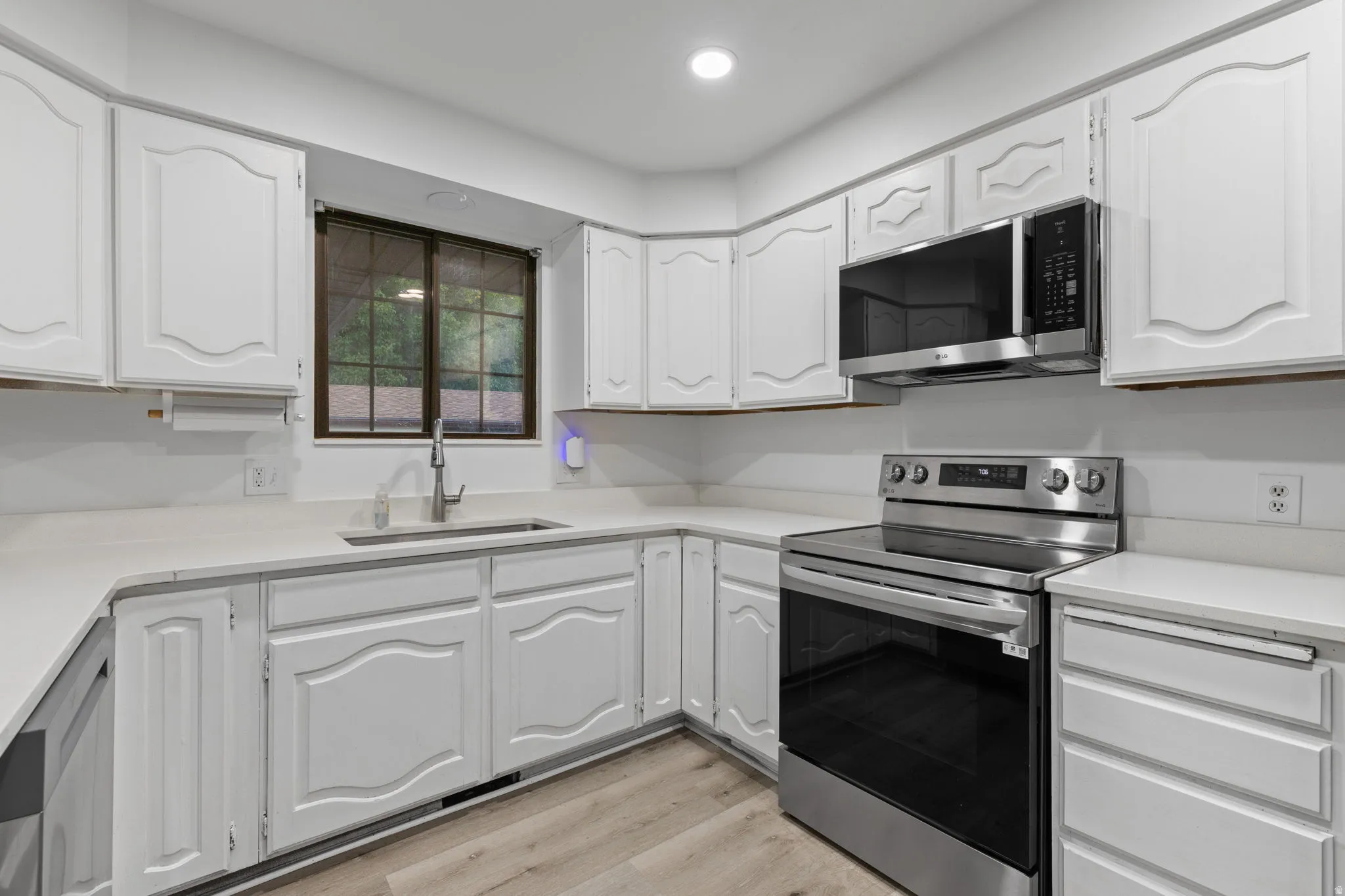 White cabinetry with decorative paneling, light countertops, stainless steel appliances, and wood-finish flooring