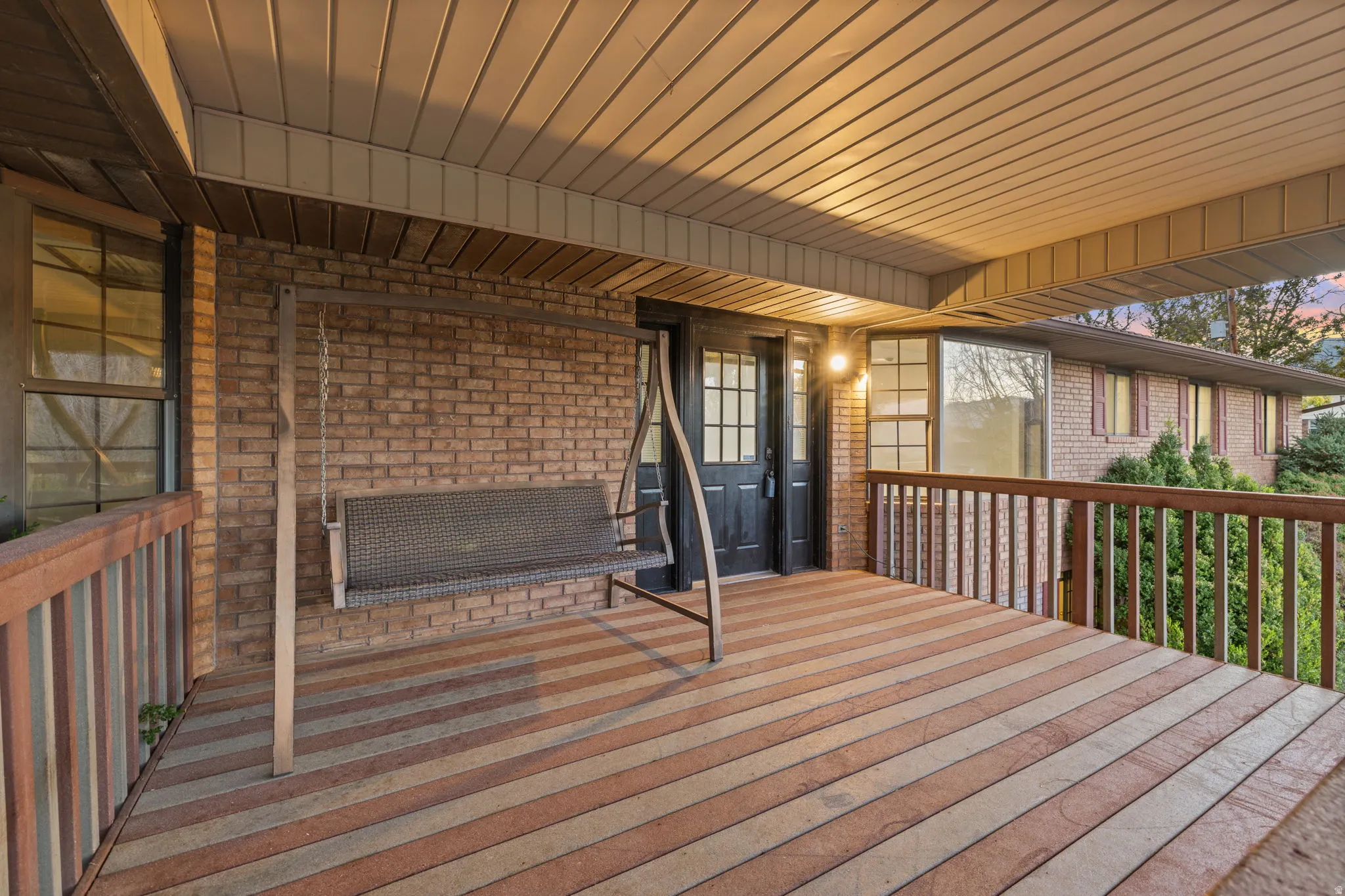 Covered porch with striped wood-finish decking, brick exterior, and wood railing