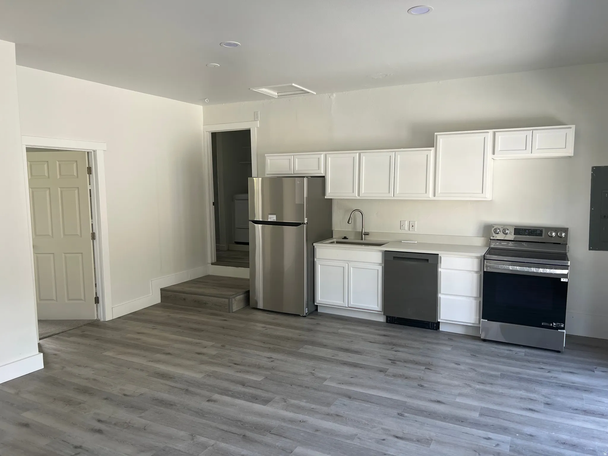 Kitchenette featuring white cabinetry, stainless steel appliances, light-toned countertops, and wood-finish flooring