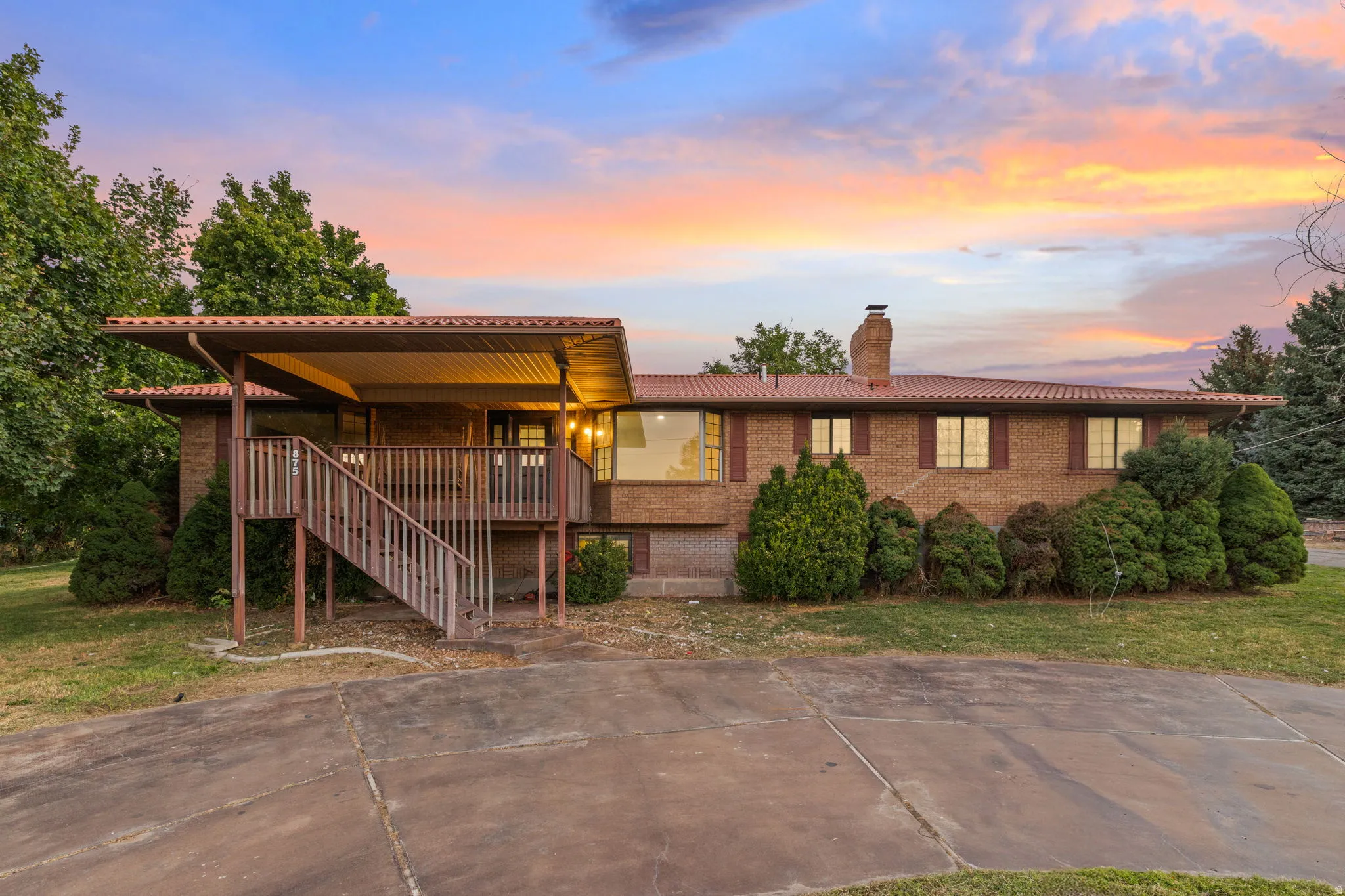Brick exterior with a tiled roof, covered deck, and an expansive driveway