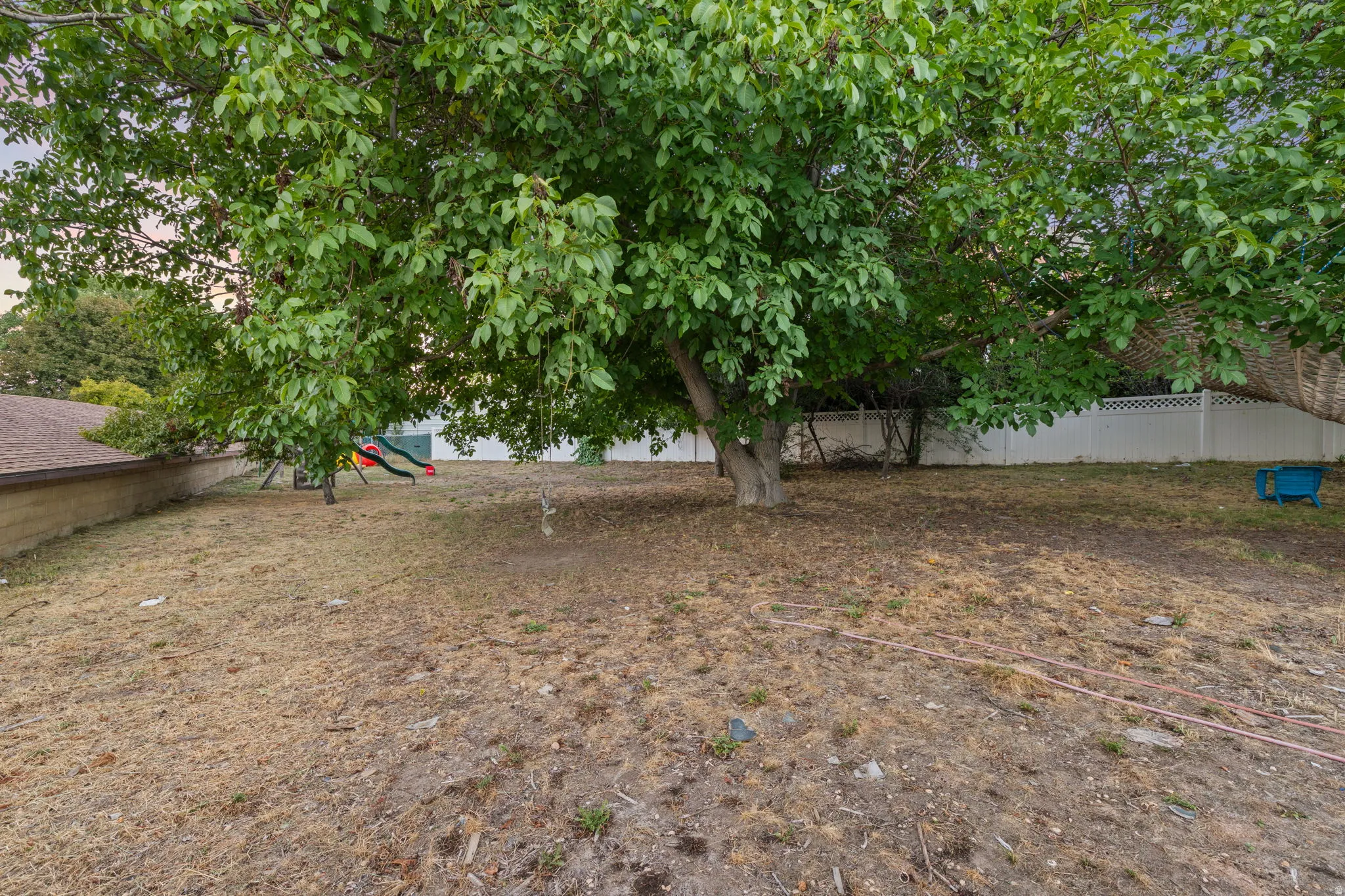 Expansive yard with a mature tree, perimeter fencing, and a sloped terrain