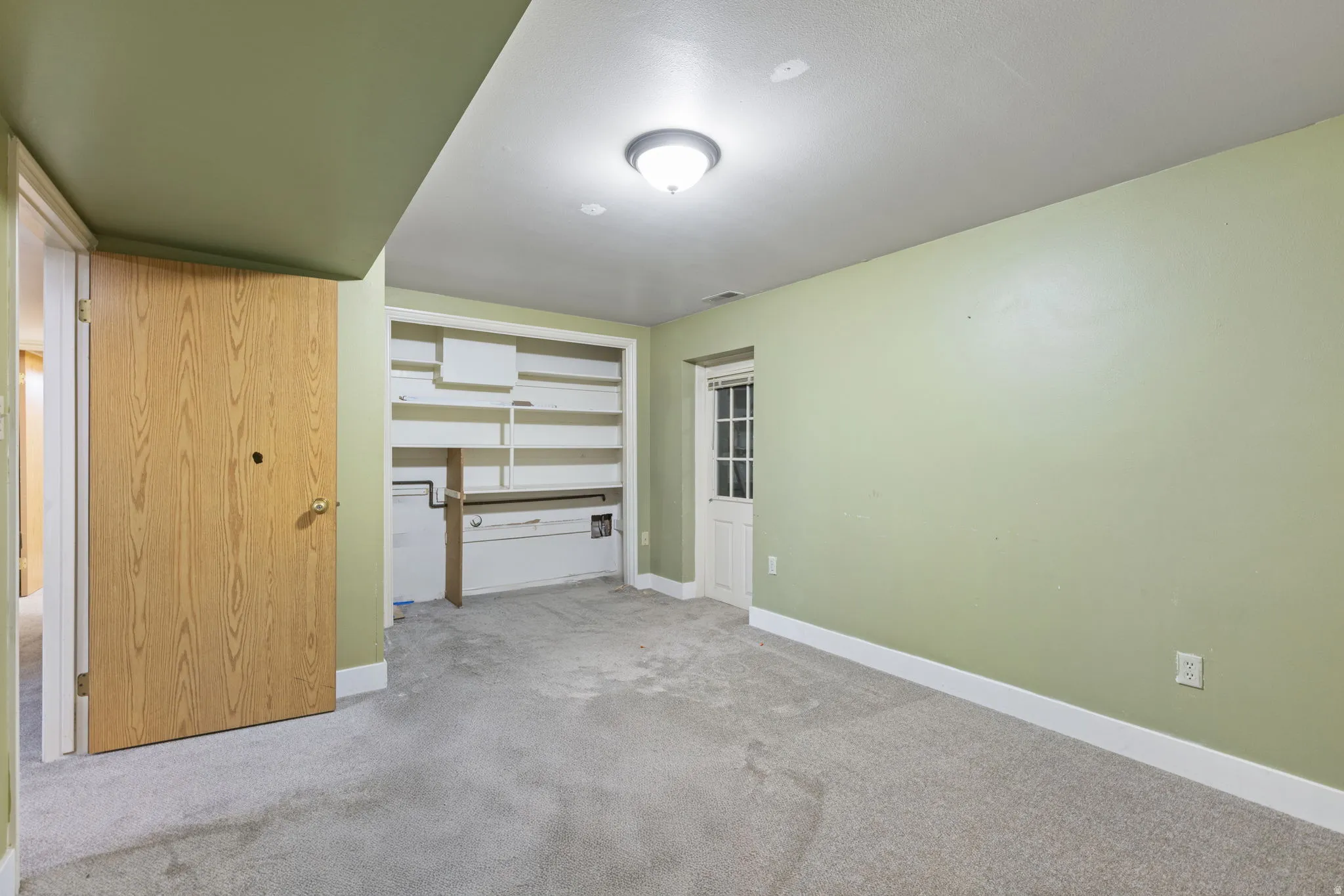 Light green walls with white trim, built-in shelving, carpet flooring, and a white paneled door with glass inserts