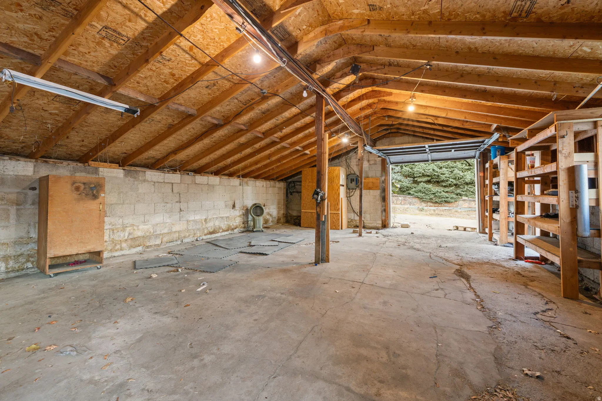 Spacious garage with exposed wood rafters, concrete flooring, block wall construction, built-in shelving, and a large overhead door