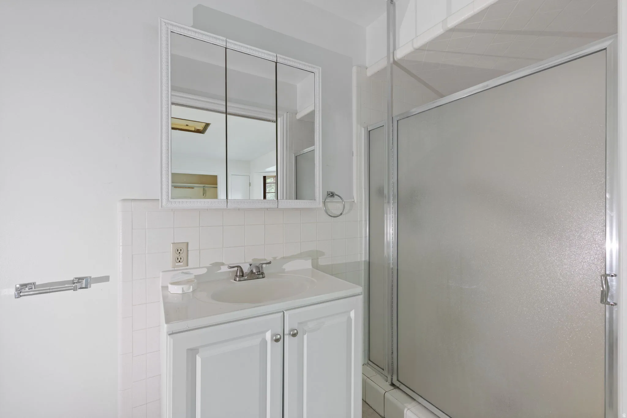 White vanity with integrated sink, chrome faucet, medicine cabinet with mirrored doors, and white subway tile backsplash
