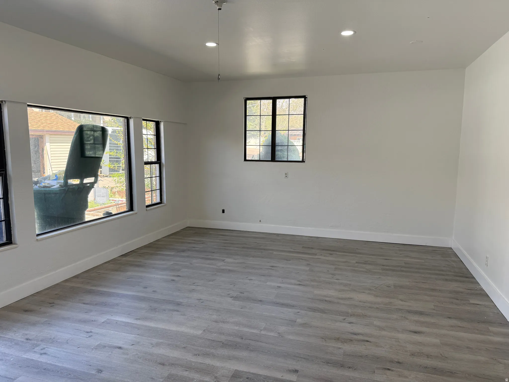 Spacious room featuring light wood-finish flooring, recessed lighting, and multiple windows with black trim