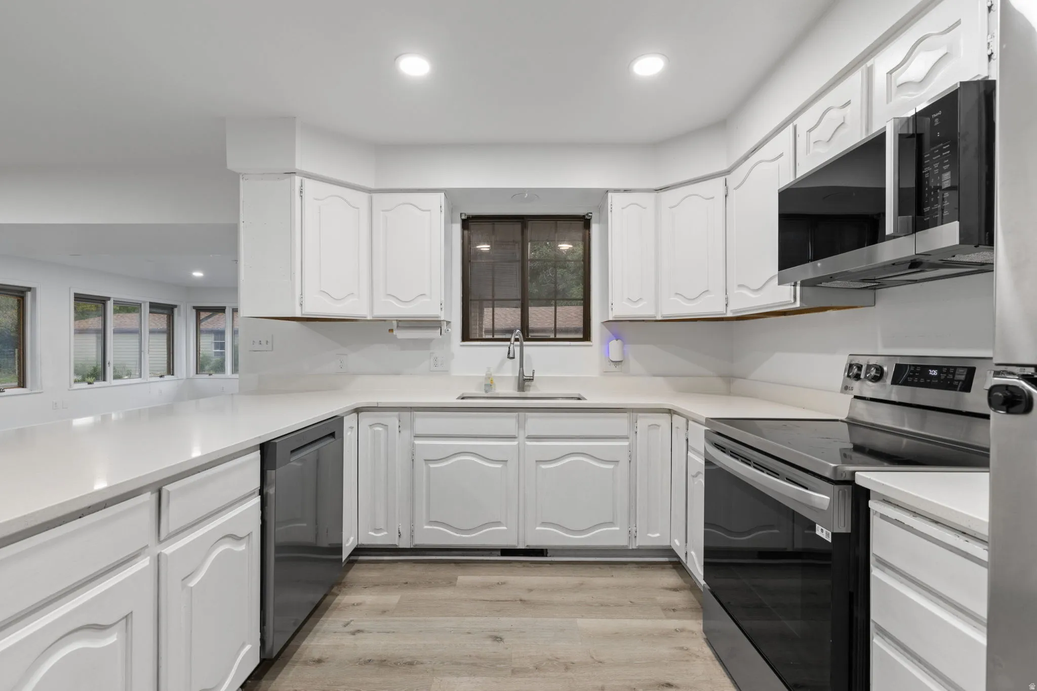 U-shaped kitchen featuring white cabinetry, light-toned countertops, and wood-finish flooring