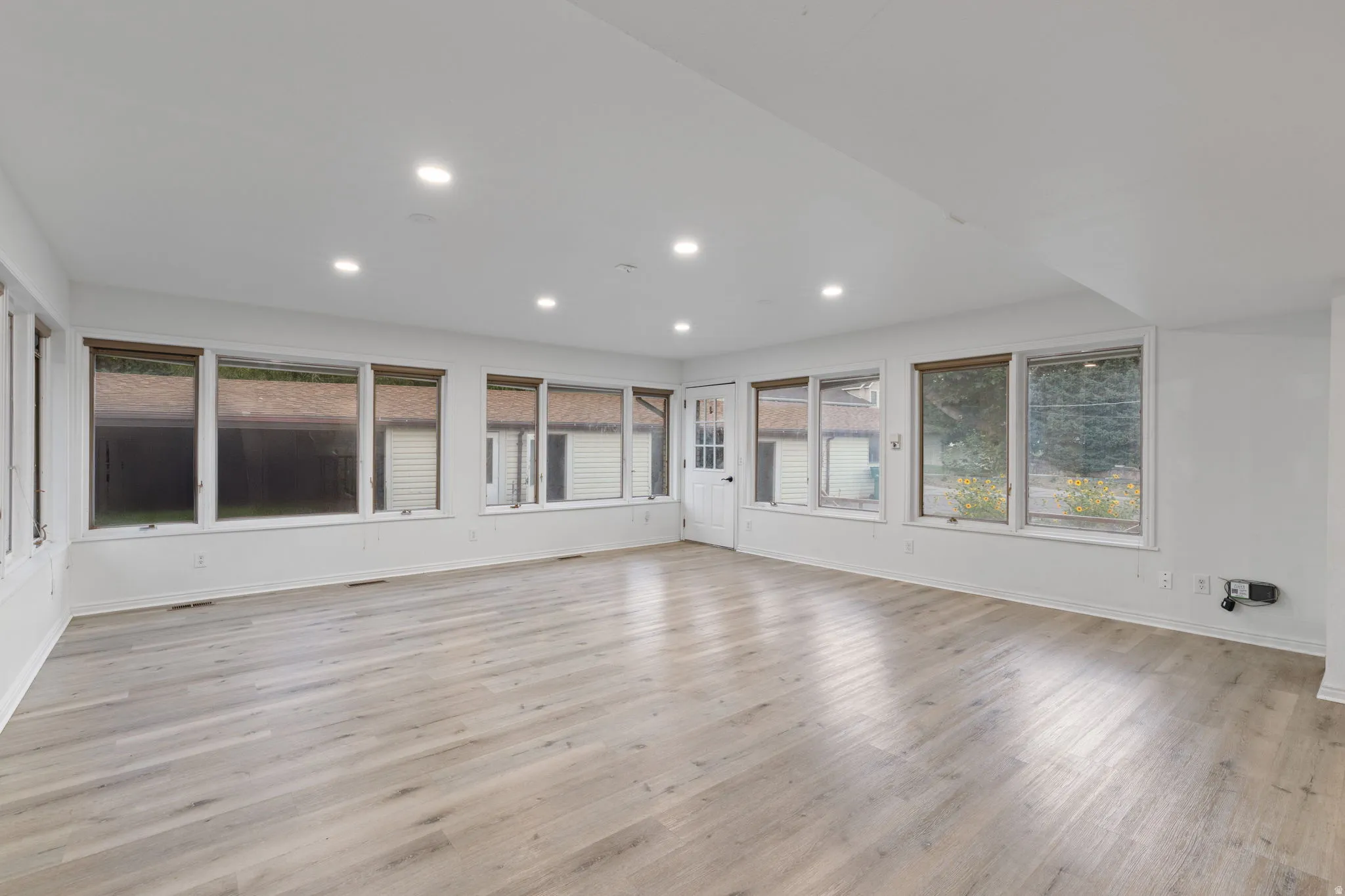 Recessed lighting, wood-finish flooring, white walls, multiple windows with blinds, and a white paneled door