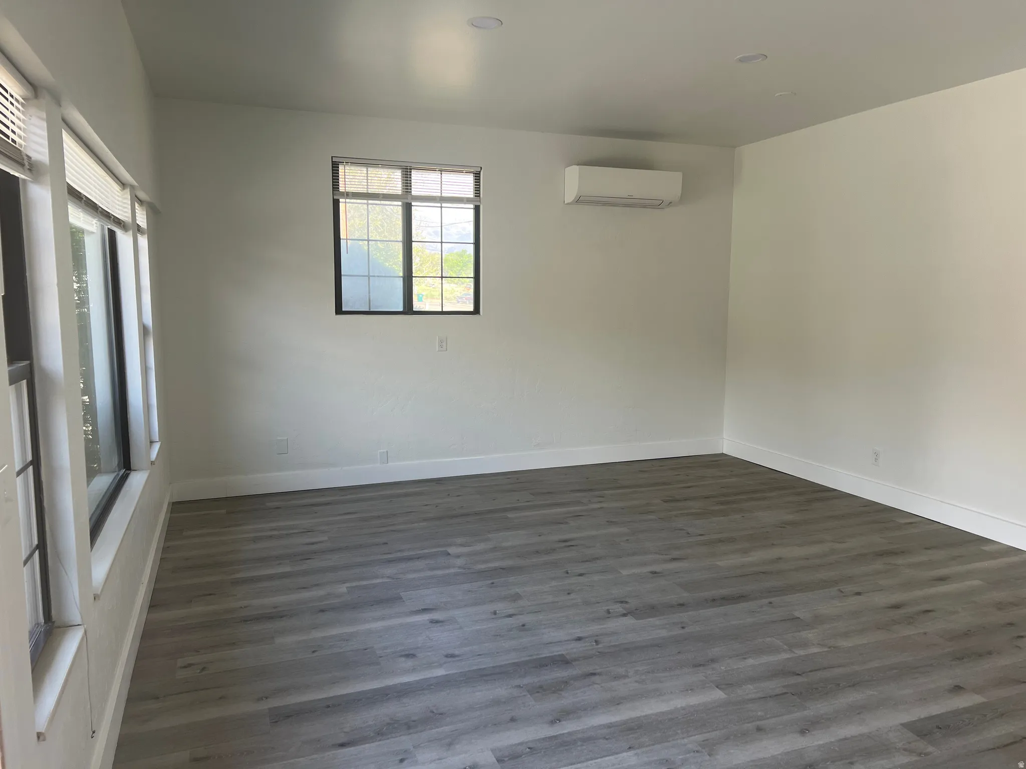Contemporary interior featuring wood-finish flooring, white walls, recessed ceiling lights, and multiple windows