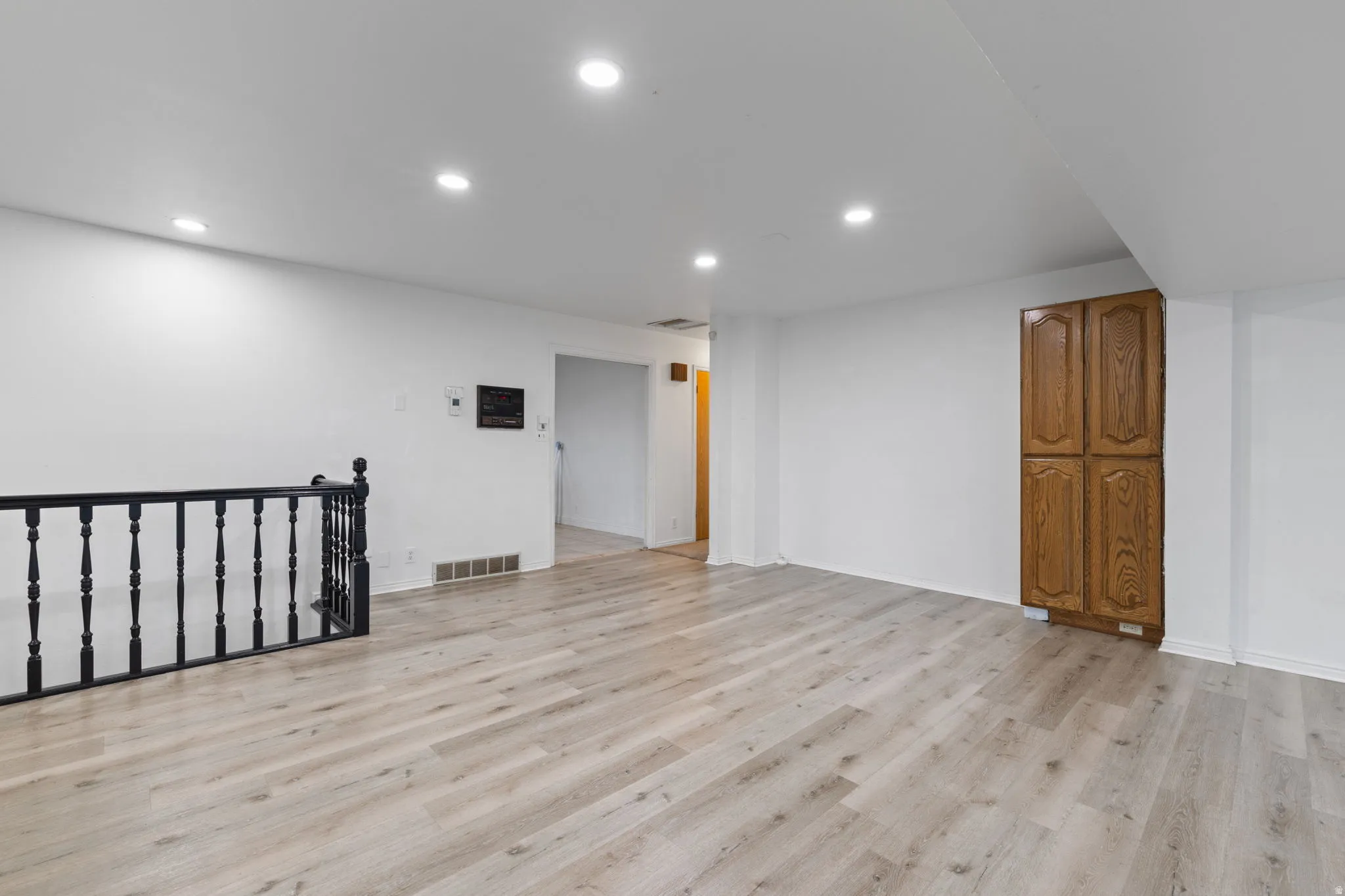 Recessed lighting illuminates the open floorplan featuring wood-finish flooring and a black spindled railing