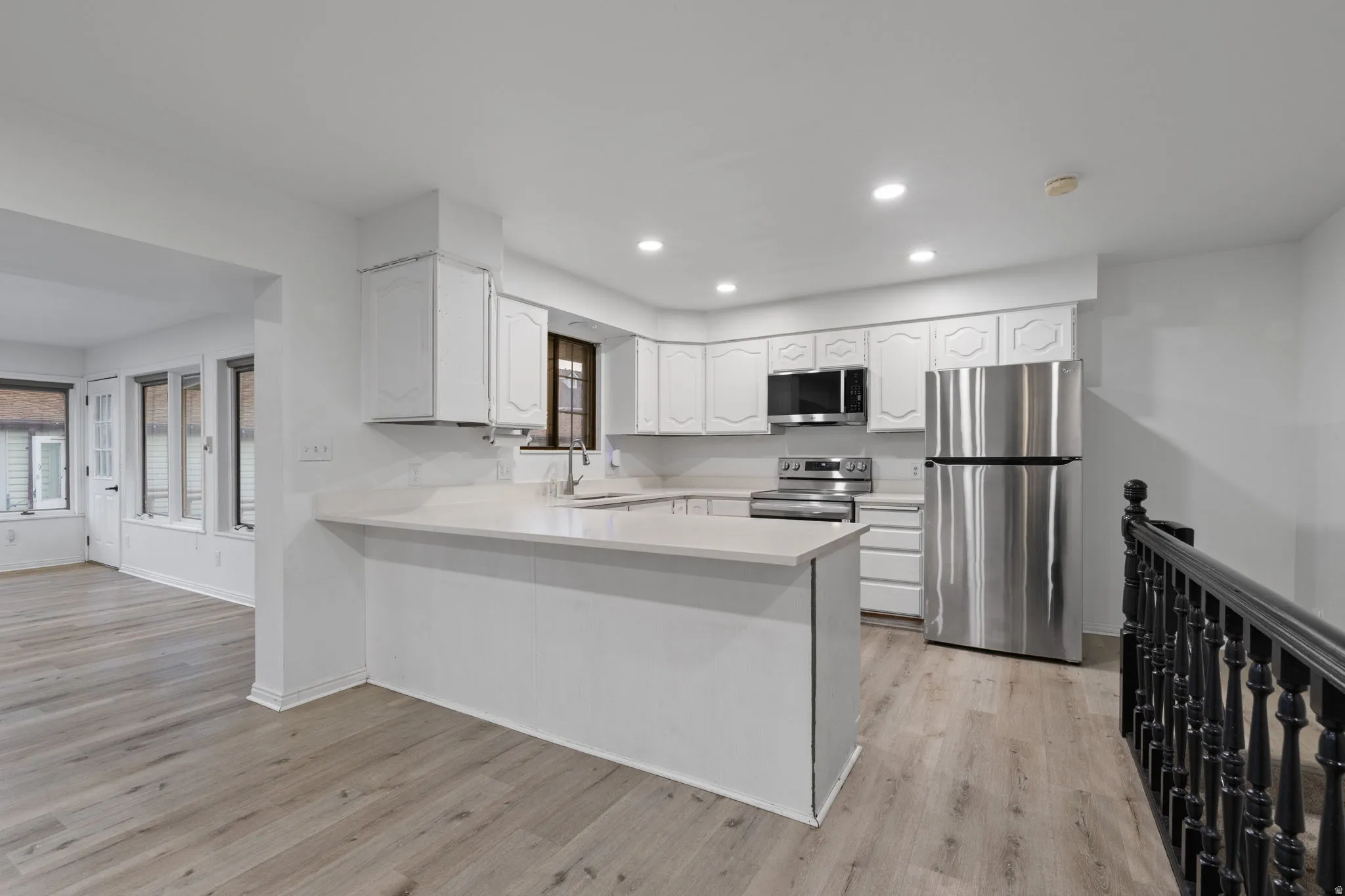 Kitchen featuring white cabinetry, stainless steel appliances, light-colored countertops, and wood-finish flooring