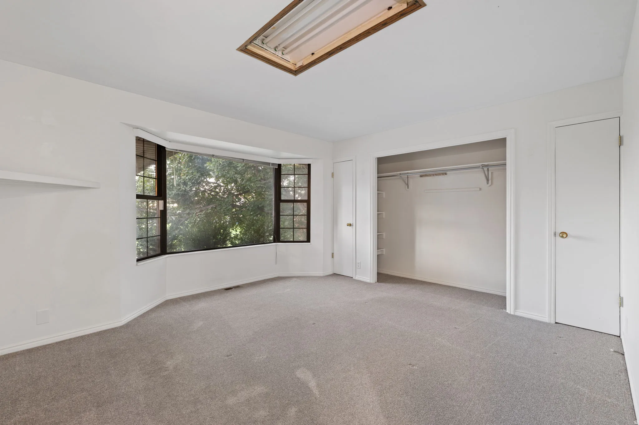 Bay window with dark-framed panes, recessed ceiling light, built-in shelving, carpeted flooring, and a closet with shelving and hanging rods