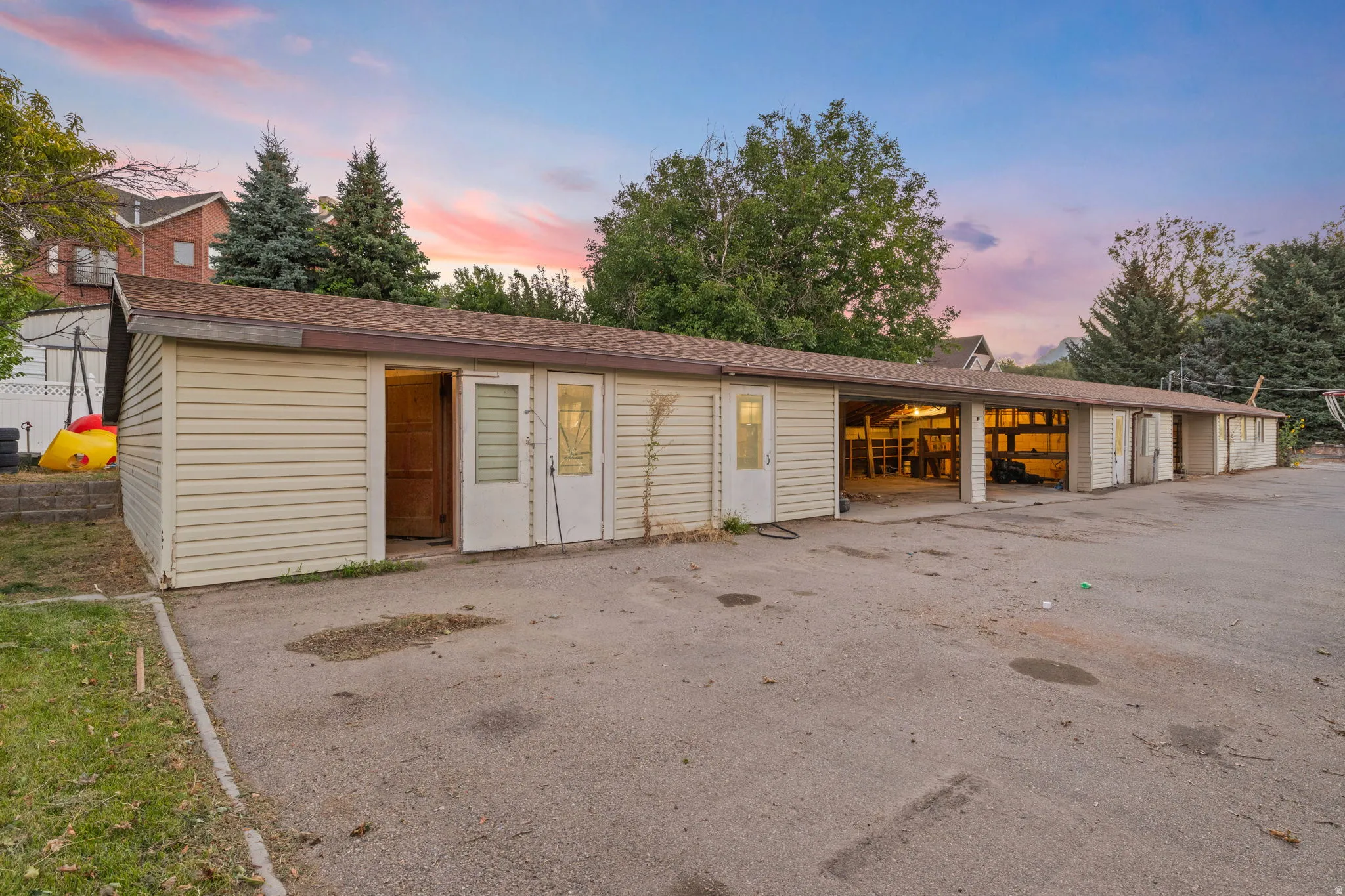 Multiple garage bays with roll-up doors, an extended paved driveway, and additional storage spaces featuring exterior doors