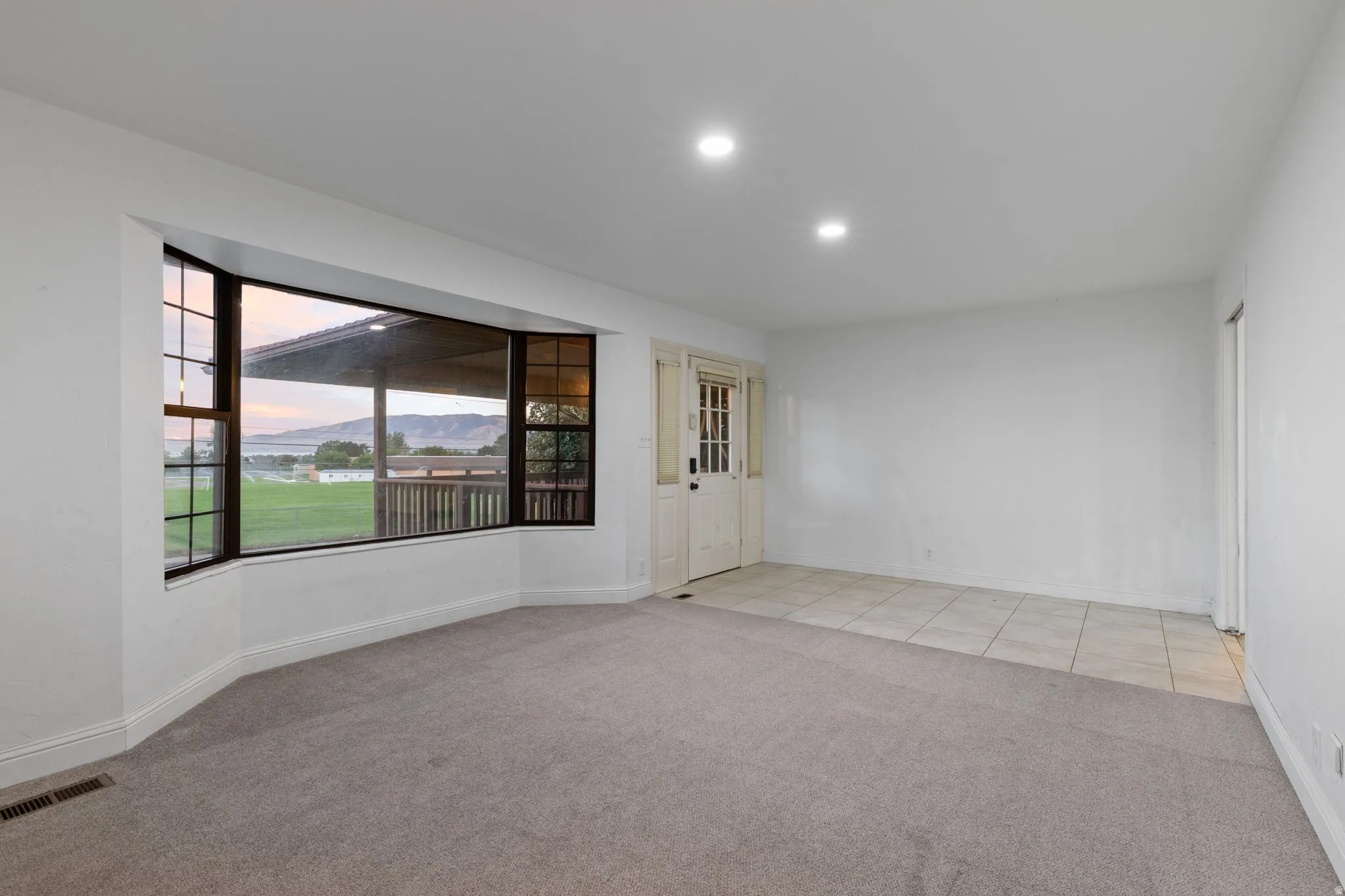 Large bay window, recessed lighting, neutral carpet, tiled entry, and a white paneled door